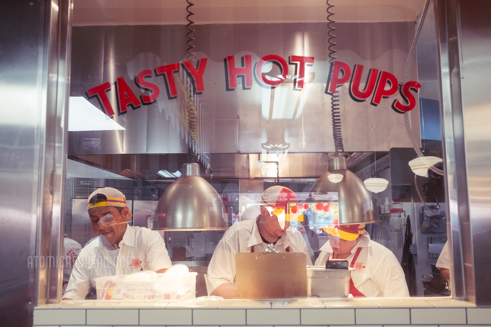 "Tasty Hot Pups" is painted in red letters on the window view to the kitchen where employees put together orders.