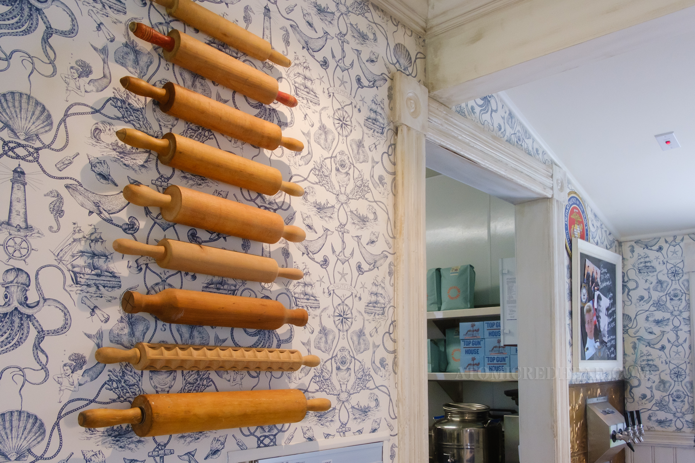 Various size rolling pins hang on a wall that is covered in blue and white wallpaper.