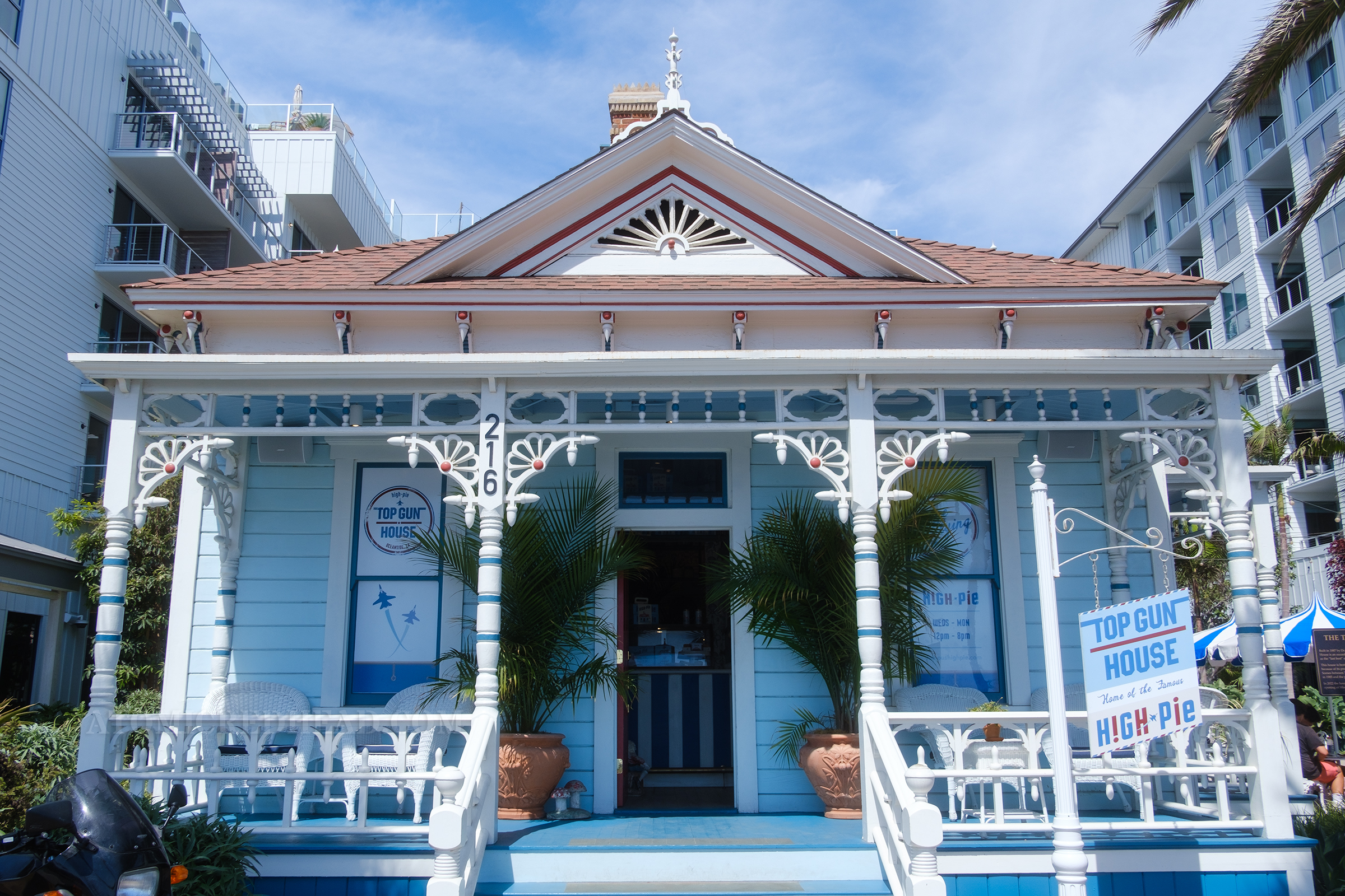 Overall view of the house, which is a small white Victorian with white gingerbread details, and elements painted in red and dark blue.