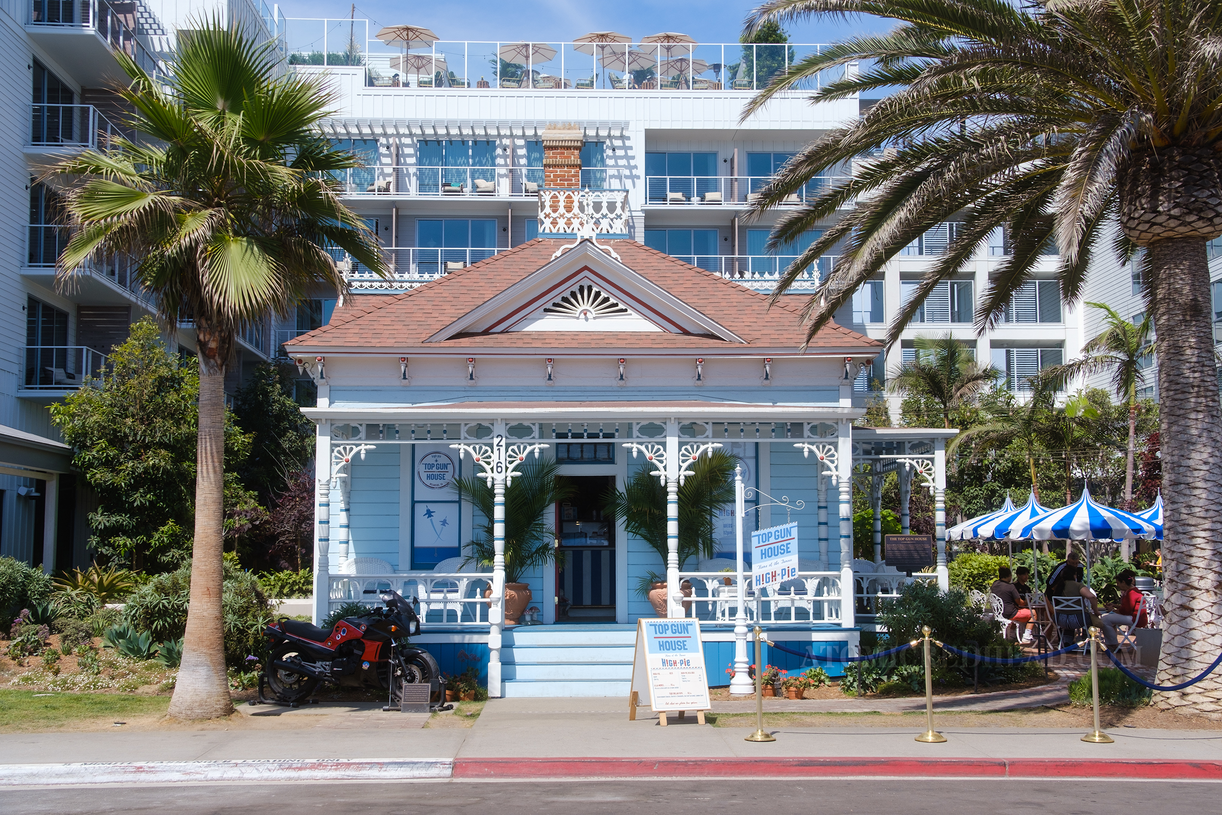Overall view of the house, which is a small white Victorian with white gingerbread details, and elements painted in red and dark blue.