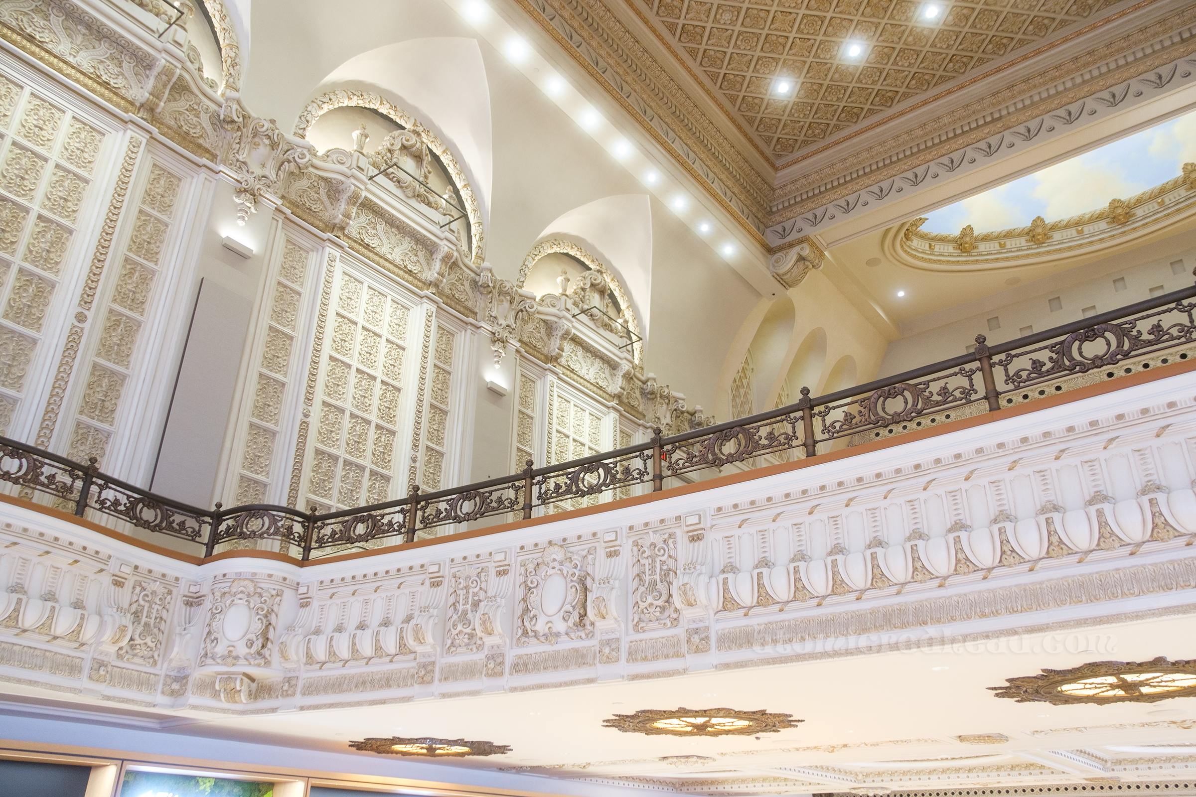 Overview of the balcony, painted in gold and white, with brass railings. 