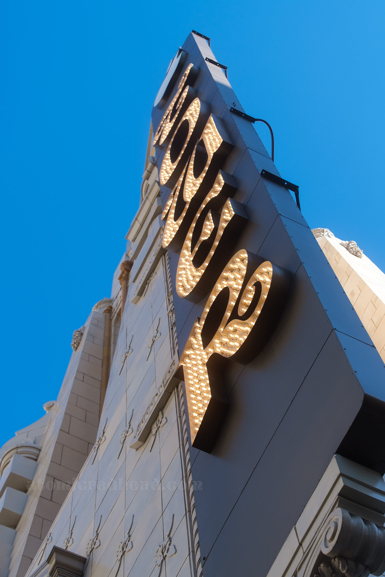 Angled view of the blade sign, which reads "TOWER" in curling letters and is lit up by small white bulbs.