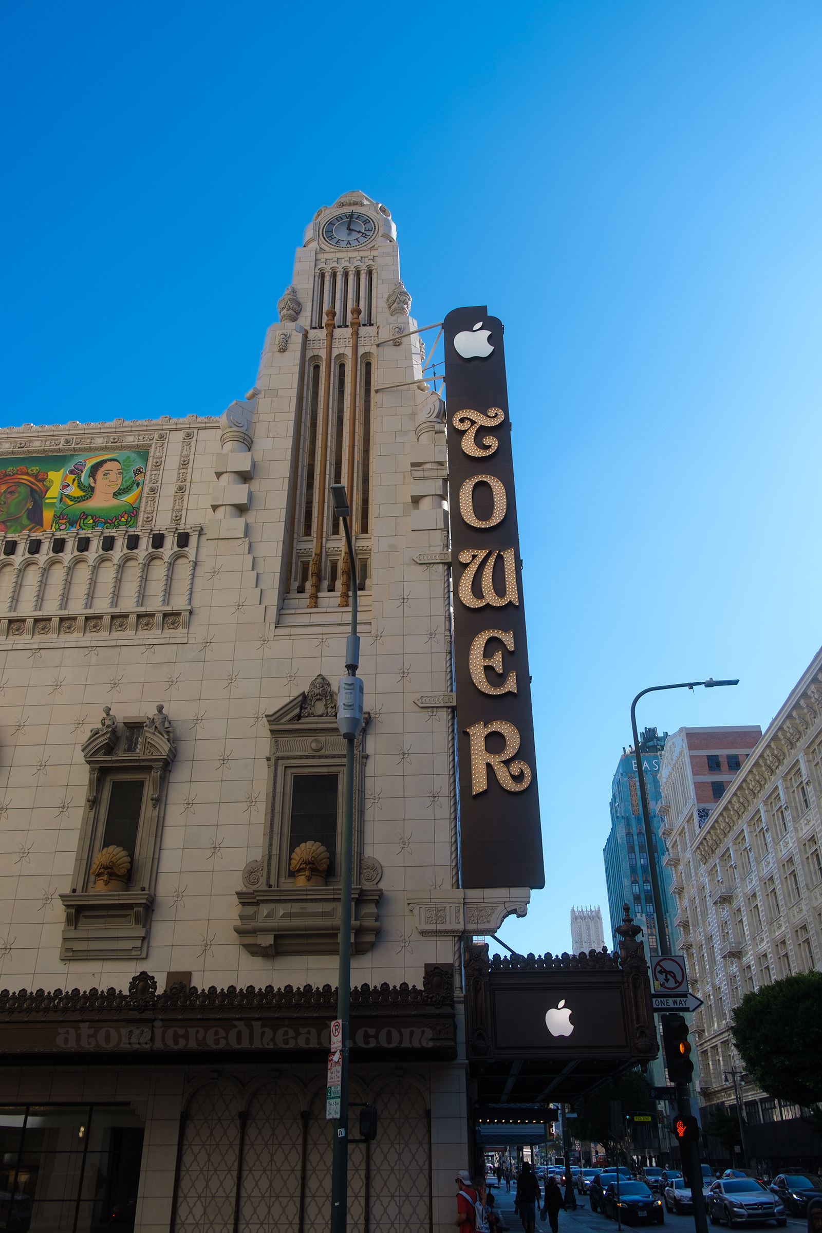 View of the theatre from the side, which has a large tall clock tower and the long blade sign hanging off the corner. 