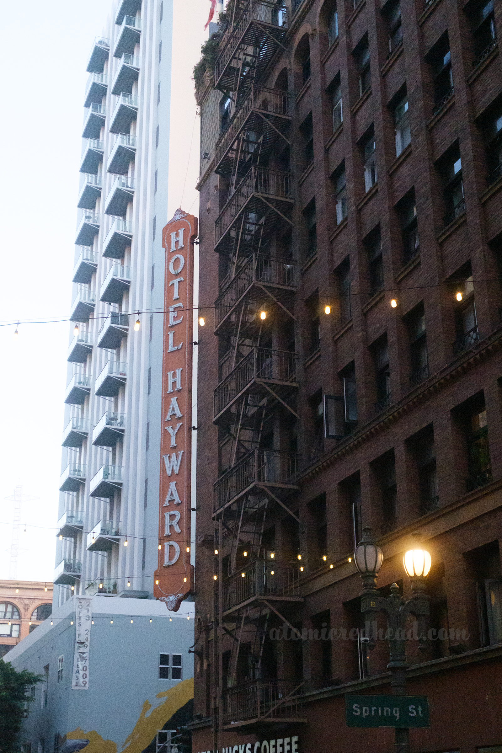 A long red blade style sign hangs off the corner of a brick building reading "Hotel Hayward"