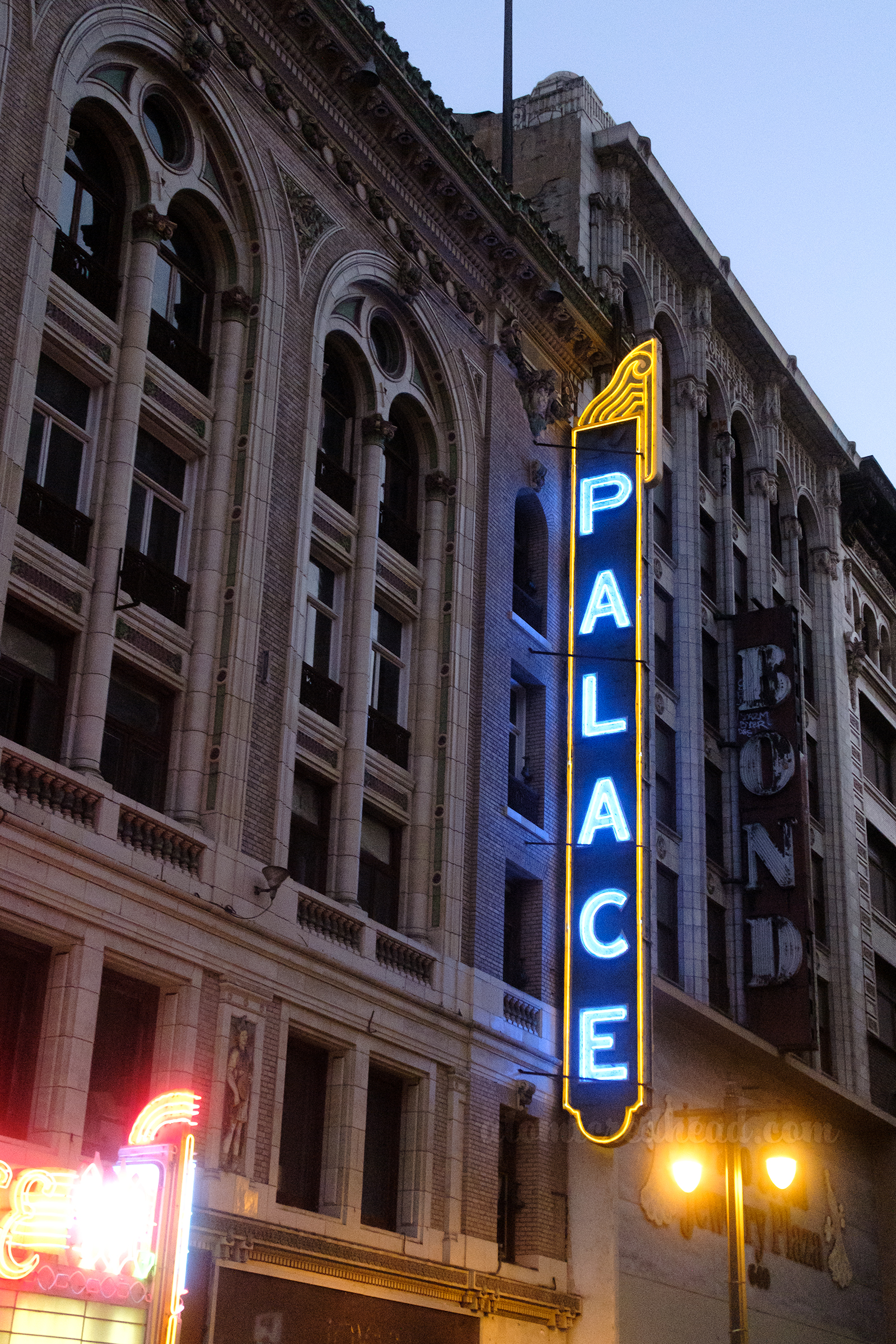 A blue blade style neon sign is edged in golden yellow neon and reads "Palace" in blue neon.