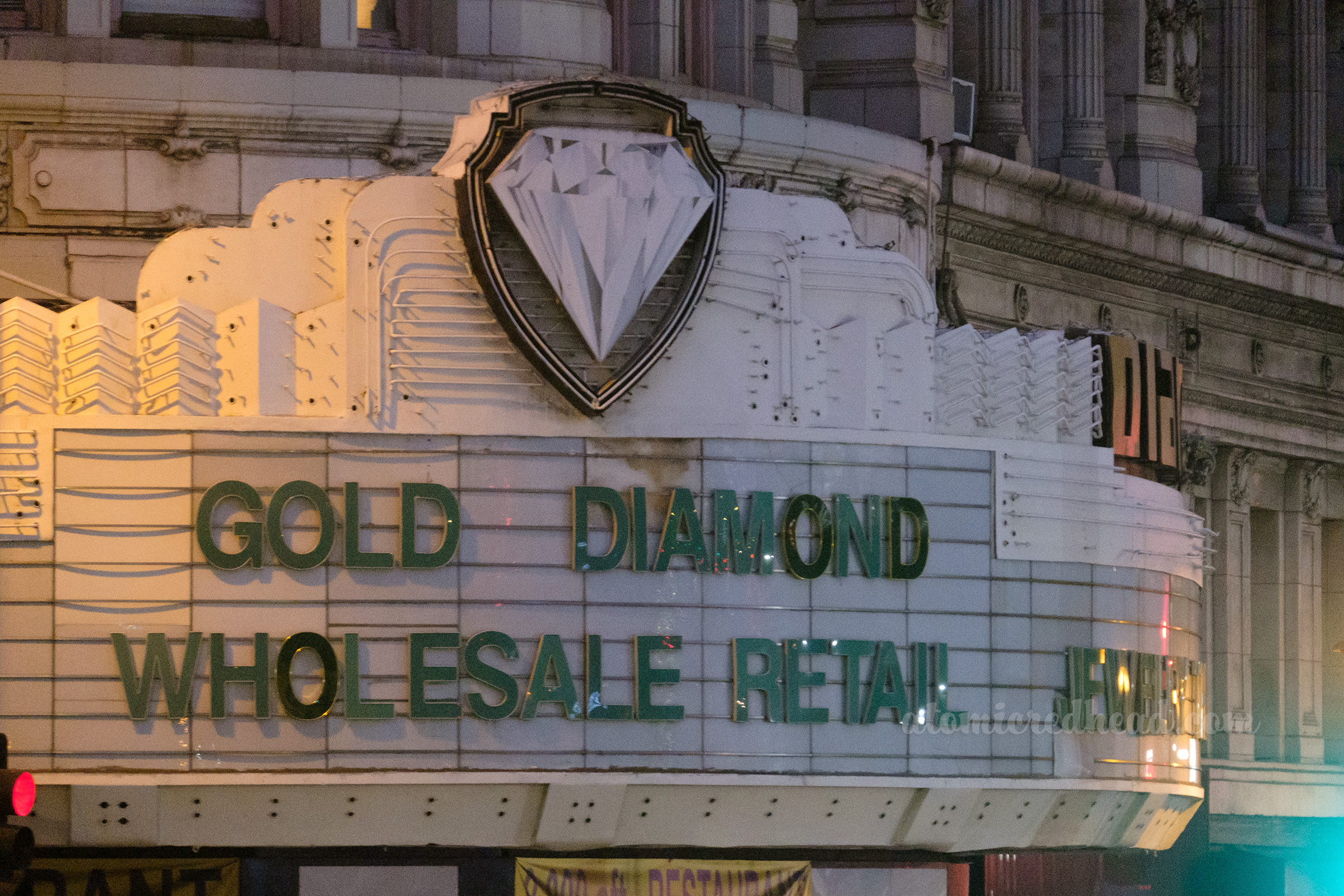 An unlit neon sign marquee of what was once a Warner Bro. theater turned diamond store, features a diamond inside the wold WB logo, and "Gold Diamond Wholesale Retail" in green letters on the marquee.