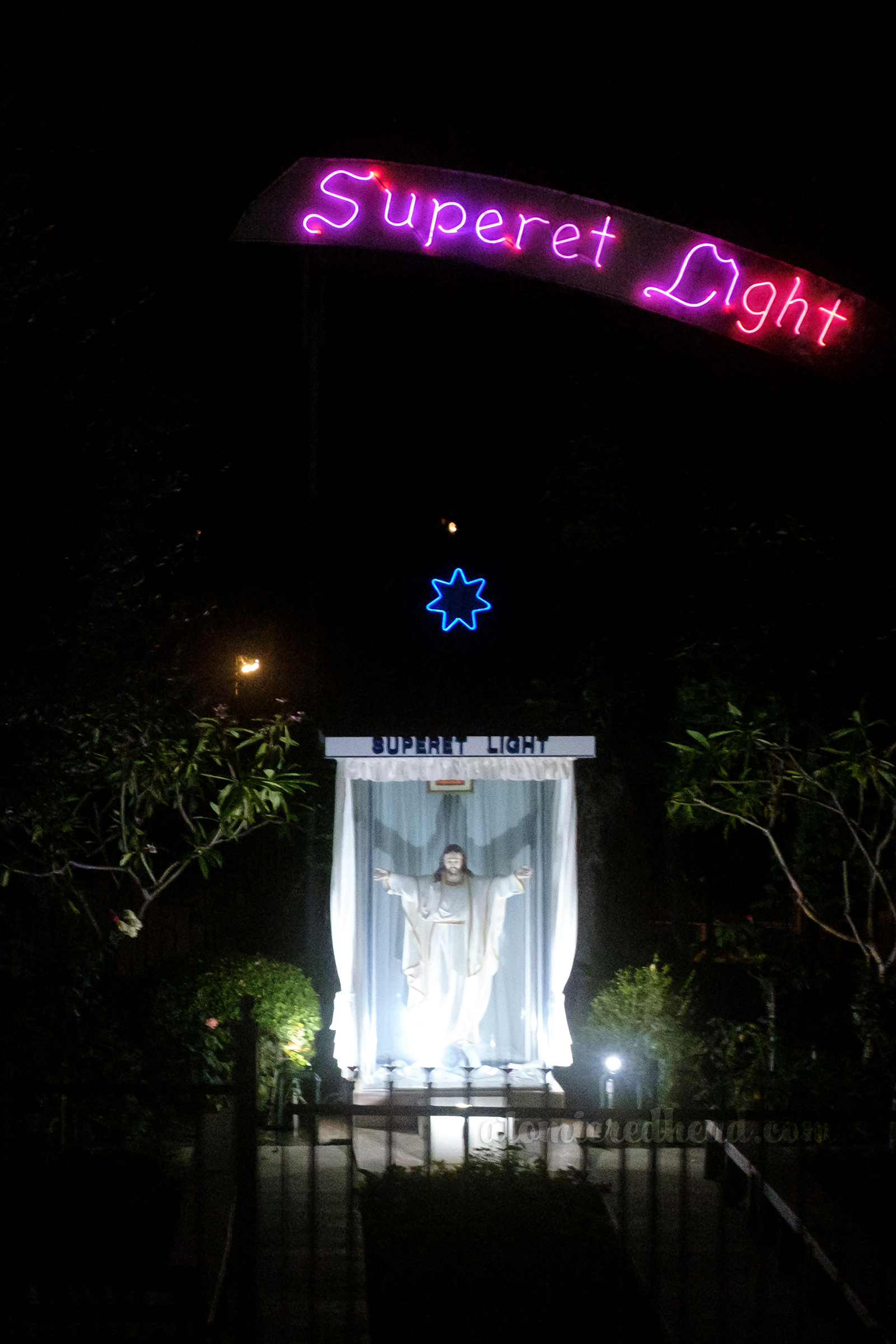 Pink neon reads "Superet Light" above a statue of Jesus.