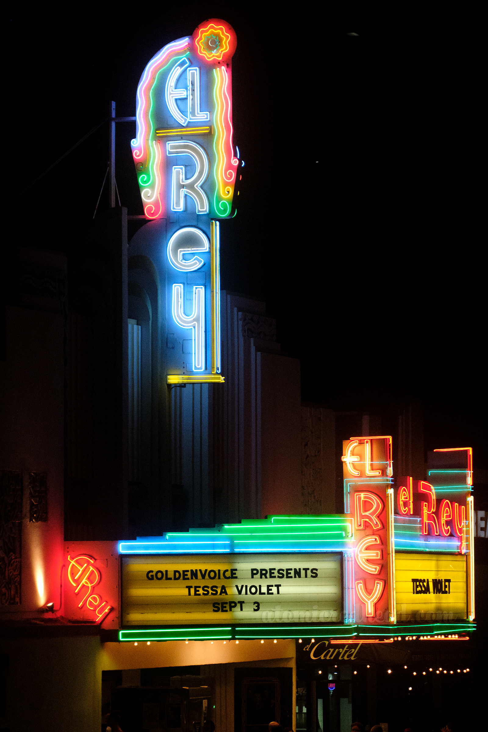 Sign and marquee for the El Rey which is various colors of neon and features artistic elements of art deco.