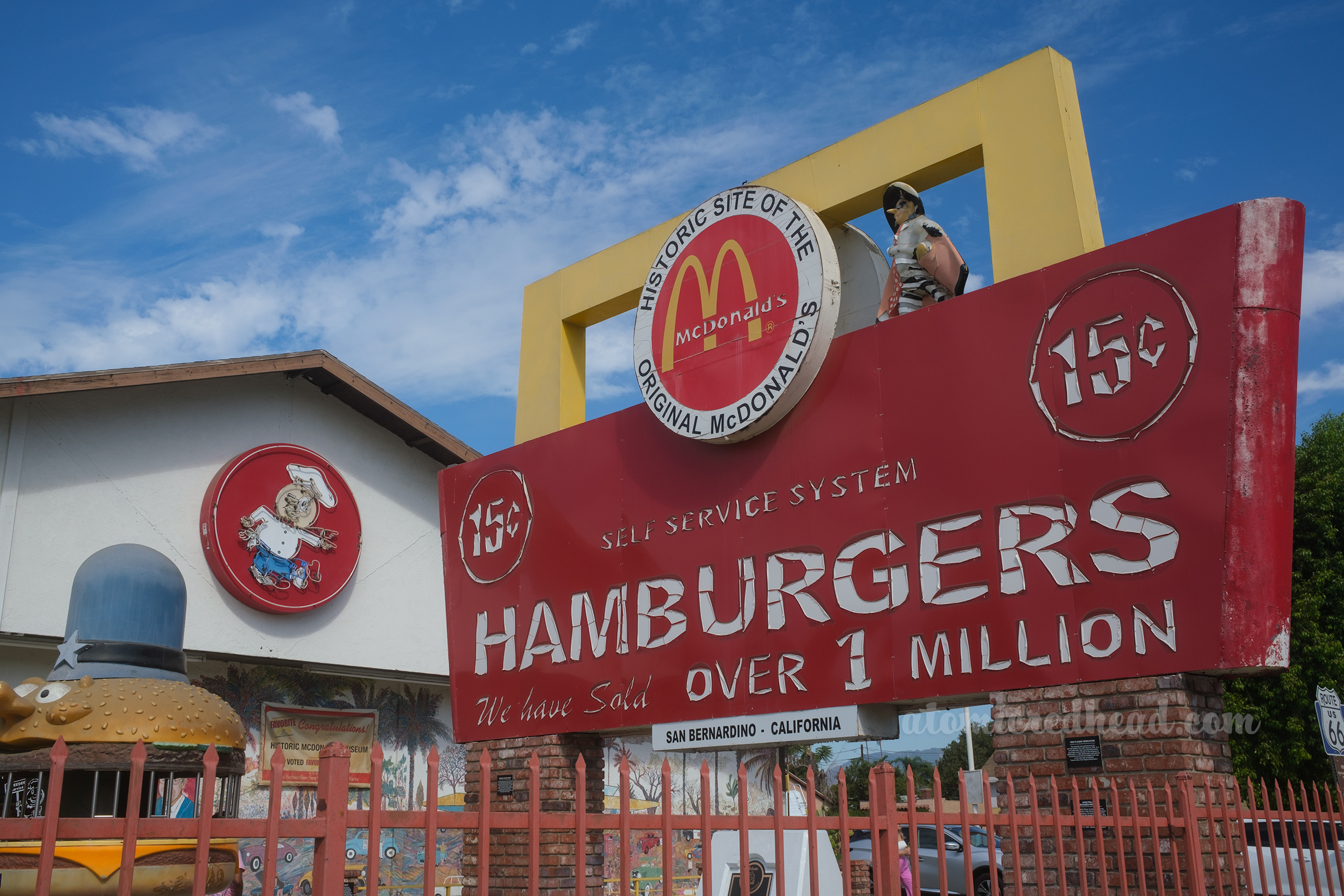 Close-up of the remains of the original sign which feature peeling white letters reading "15 cent Hamburgers Self Service System We have sold over 1 million" and a large circle with the McDonald's logo and black text reading "Historic Site of the Original McDonald's"