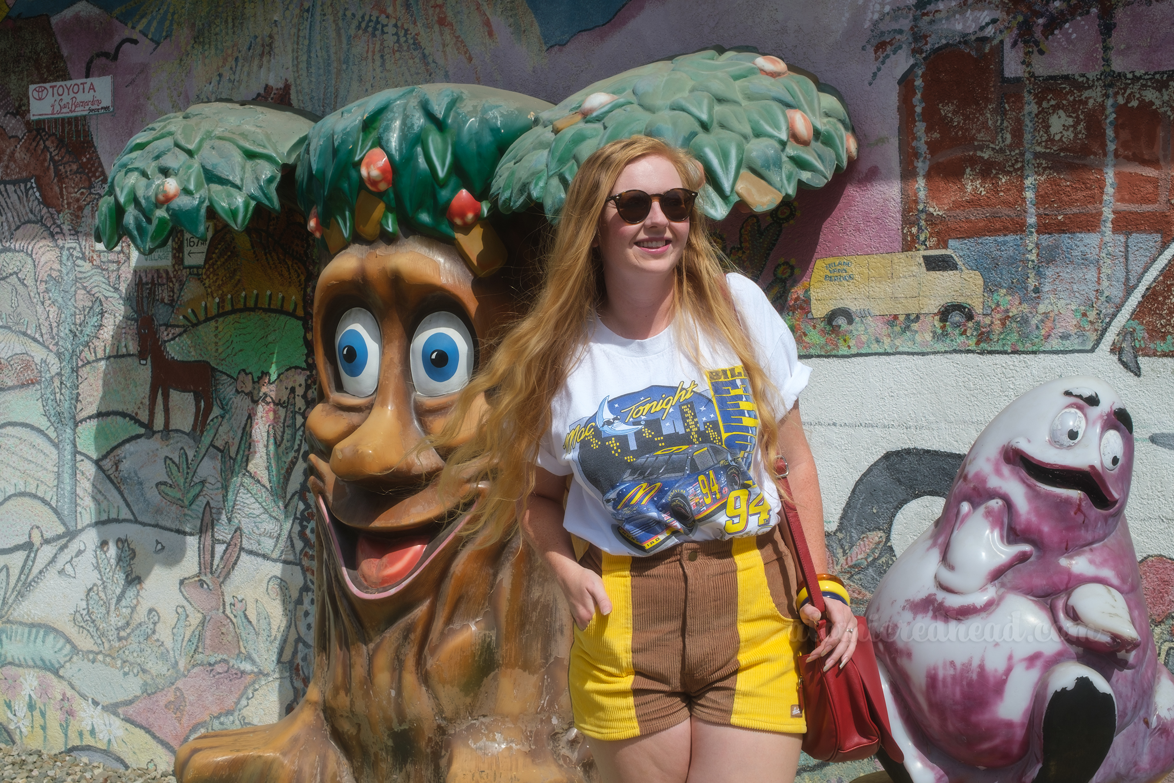 Myself standing next to a large tree with a face and a Grimace see-saw, wearing a Bill Elliot racing tee, and brown and yellow shorts.