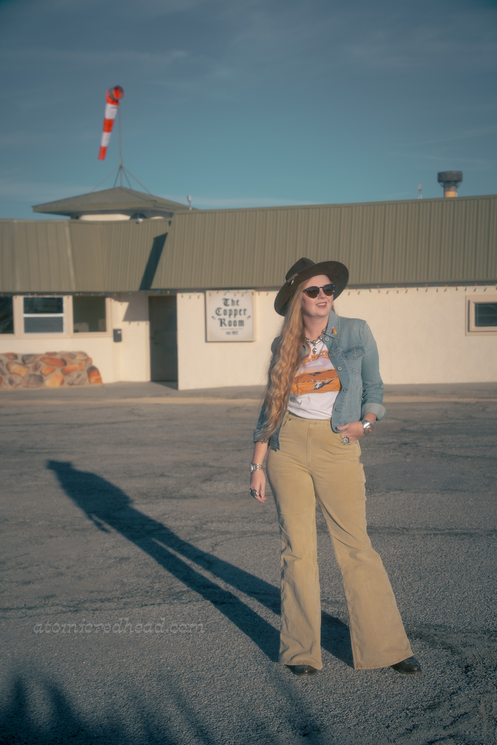Myself, wearing a brown hat, blue jean jacket, tee featuring a desert landscape, tan corduroy pants, and dark brown boots, standing in front of the Copper Room.