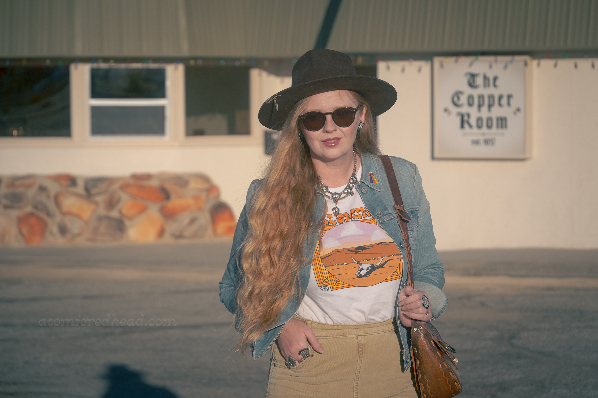 Myself, wearing a brown hat, blue jean jacket, tee featuring a desert landscape, tan corduroy pants, and dark brown boots, standing in front of the Copper Room.