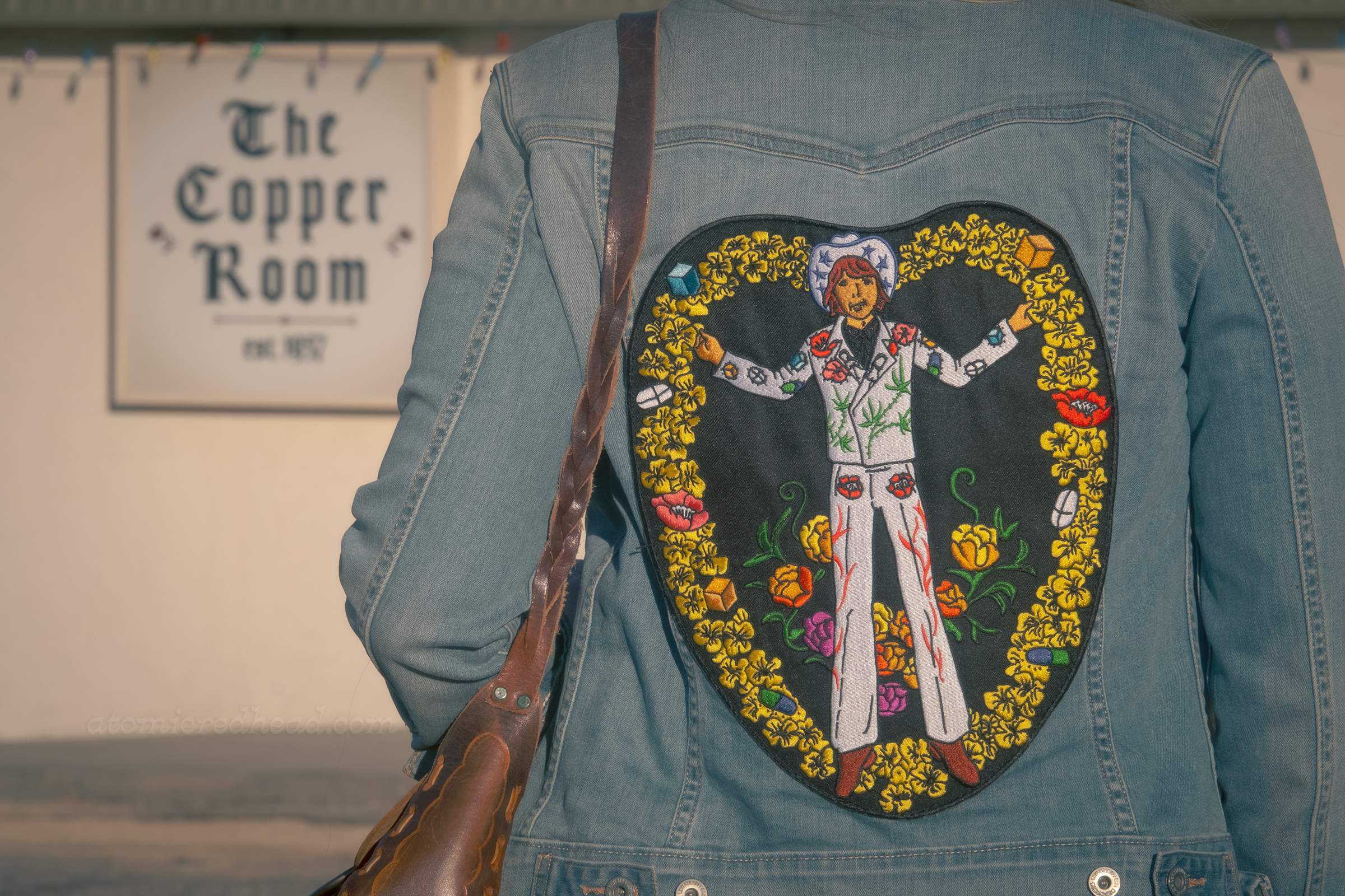 Close-up of my jacket patch, which features an embroidered Gram Parsons, wearing his white Nudie suit of pot leaves, flowers, flames, and pills, surrounded by yellow flowers, and pills, inspired by the Byrds album cover, Sweetheart of the Rodeo, which features a cowgirl in the same pose and surrounded by flowers.