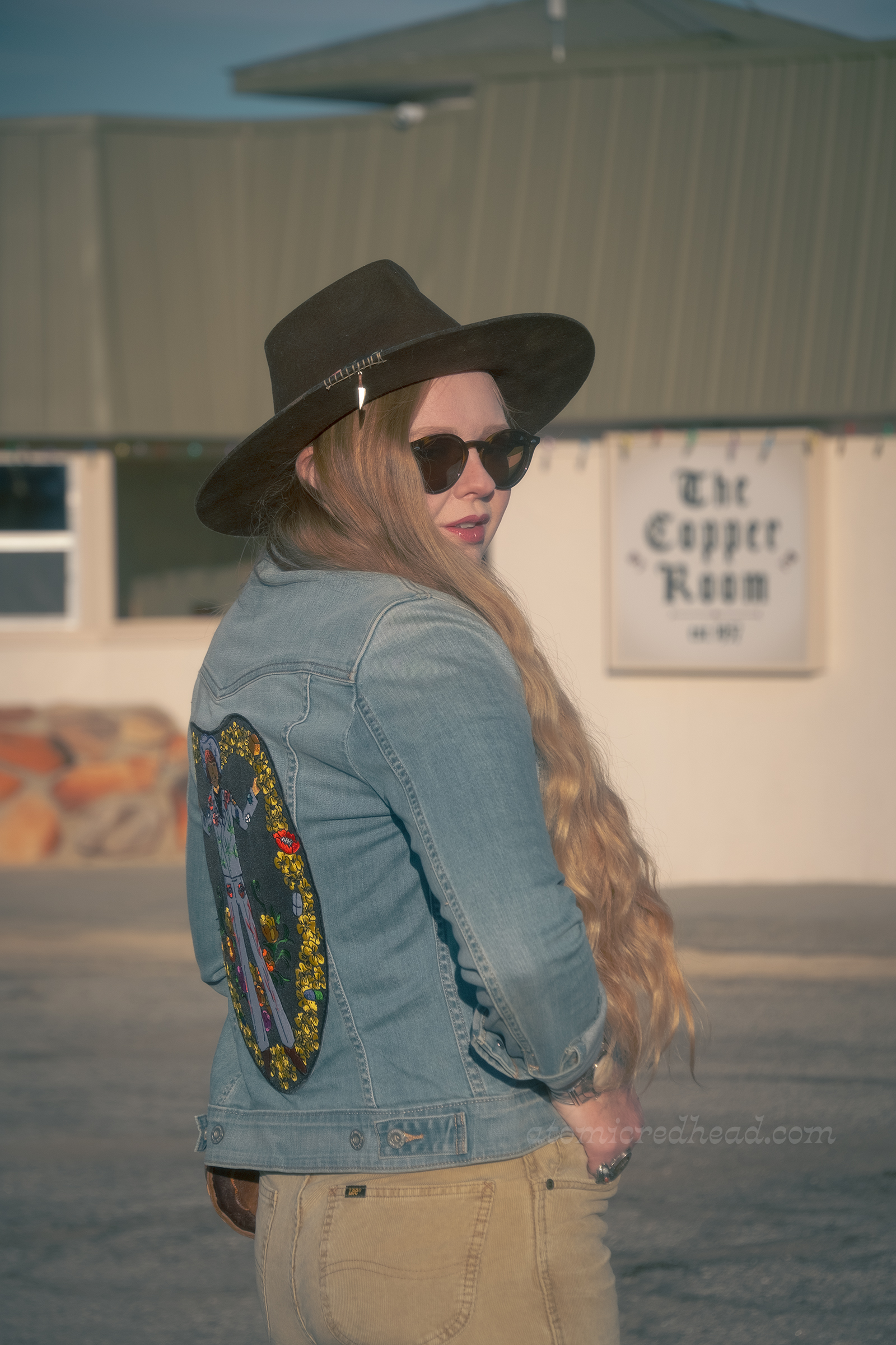 Myself, wearing a brown hat, blue jean jacket, tee featuring a desert landscape, tan corduroy pants, and dark brown boots, standing in front of the Copper Room.