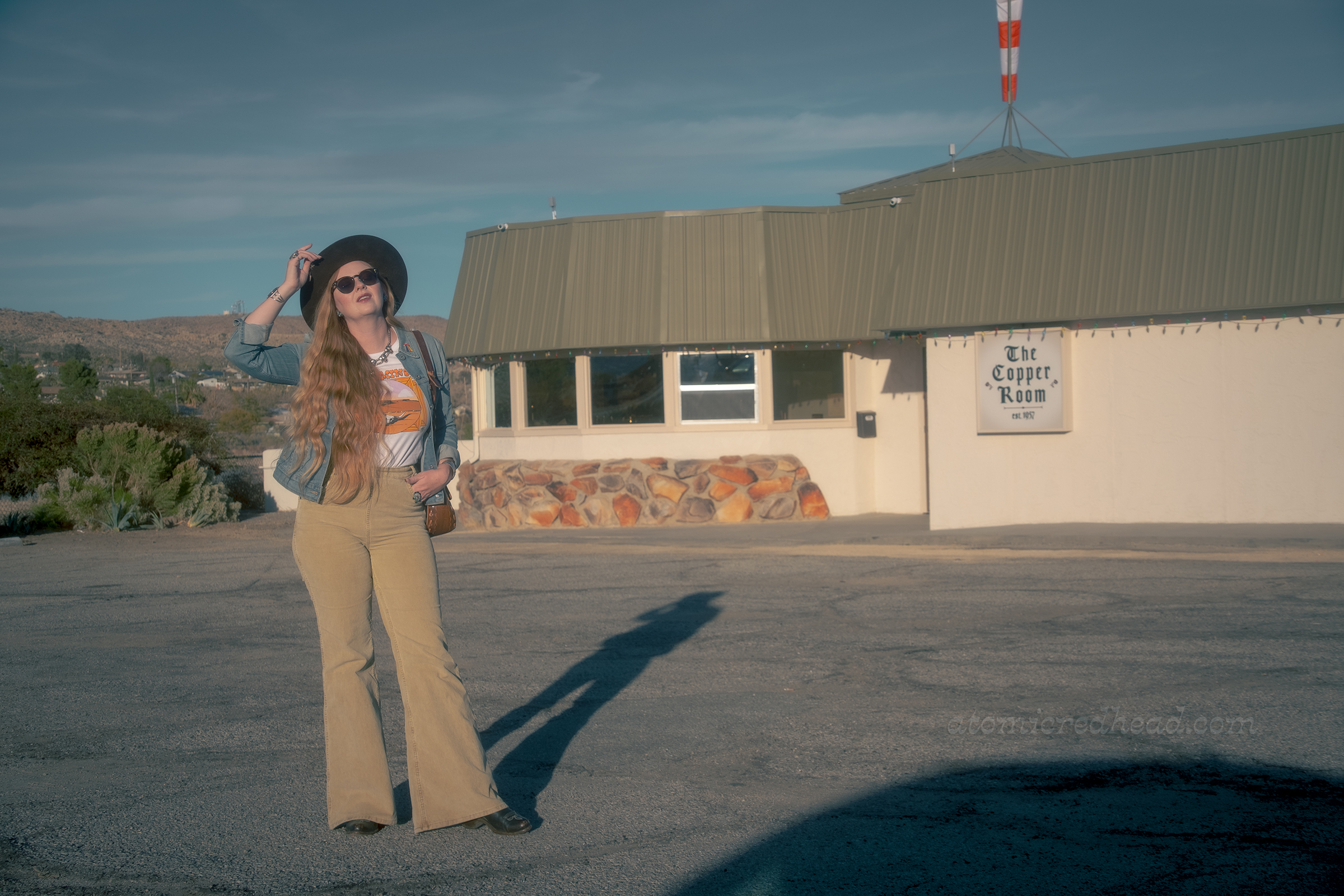 Myself, wearing a brown hat, blue jean jacket, tee featuring a desert landscape, tan corduroy pants, and dark brown boots, standing in front of the Copper Room.