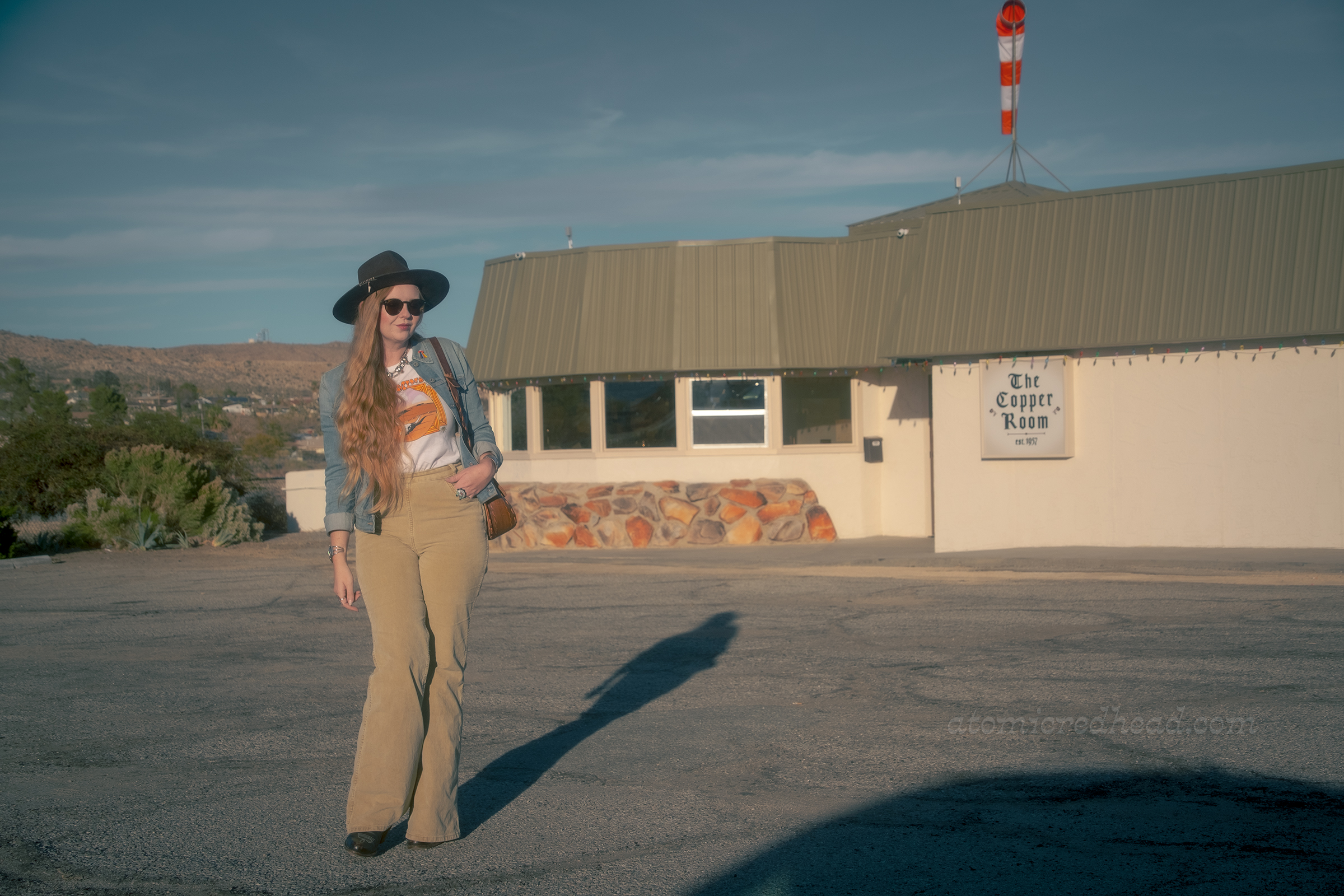 Myself, wearing a brown hat, blue jean jacket, tee featuring a desert landscape, tan corduroy pants, and dark brown boots, standing in front of the Copper Room.