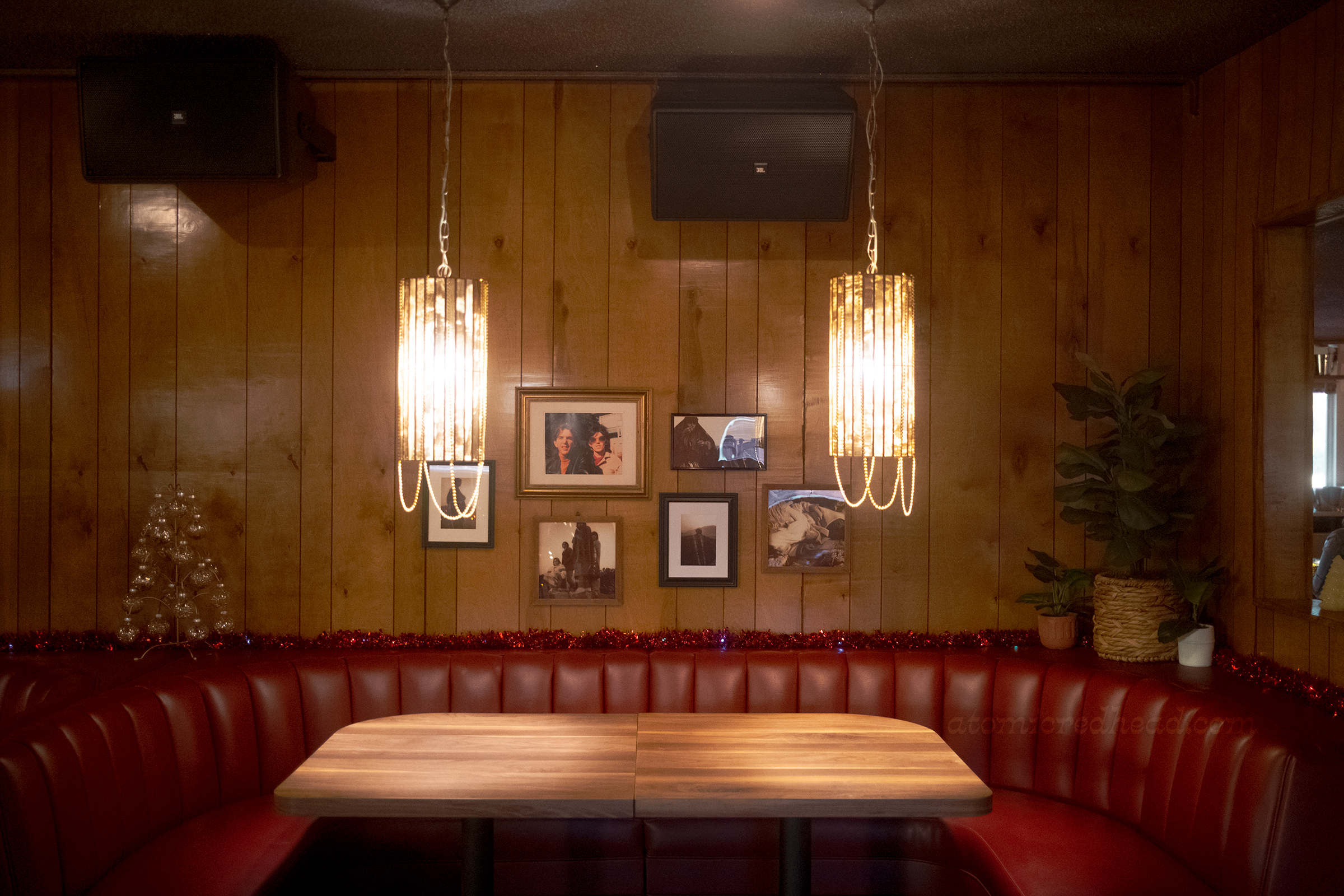 Photographs of Gram Parsons hang on a wood paneled wall, below a red leather tufted booth.