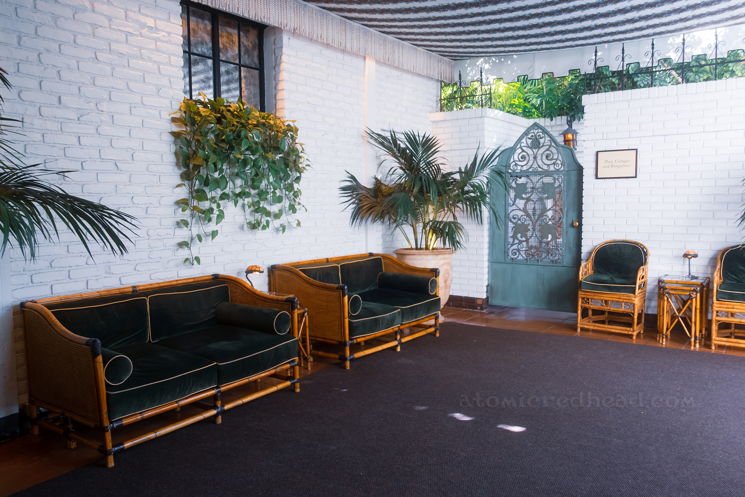 The entry area outside which features bamboo couches with dark green upholstery. A light green metal gate marks the entrance to the pool area.