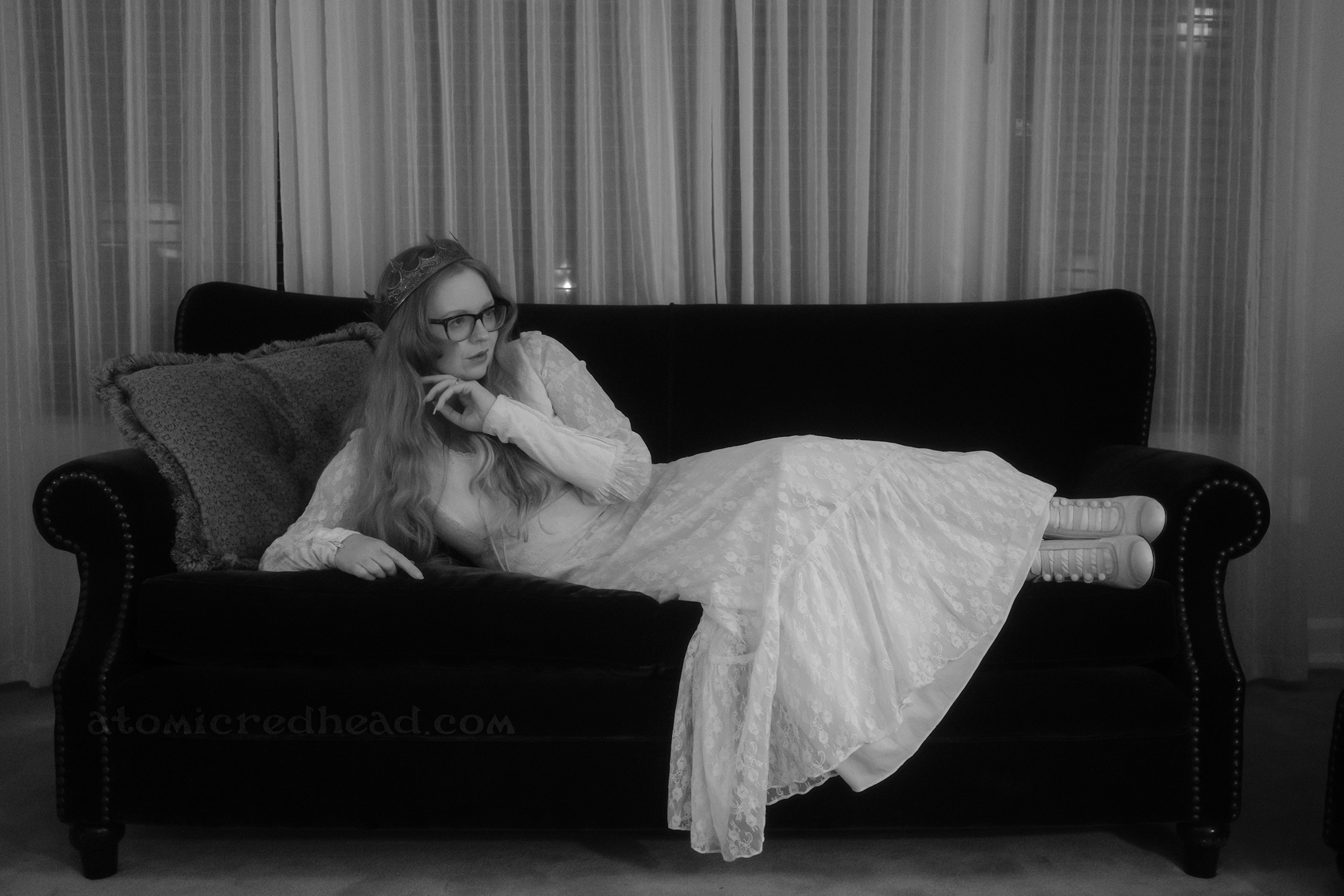 Myself, wearing a crown and a white lace dress laying on a dark couch.