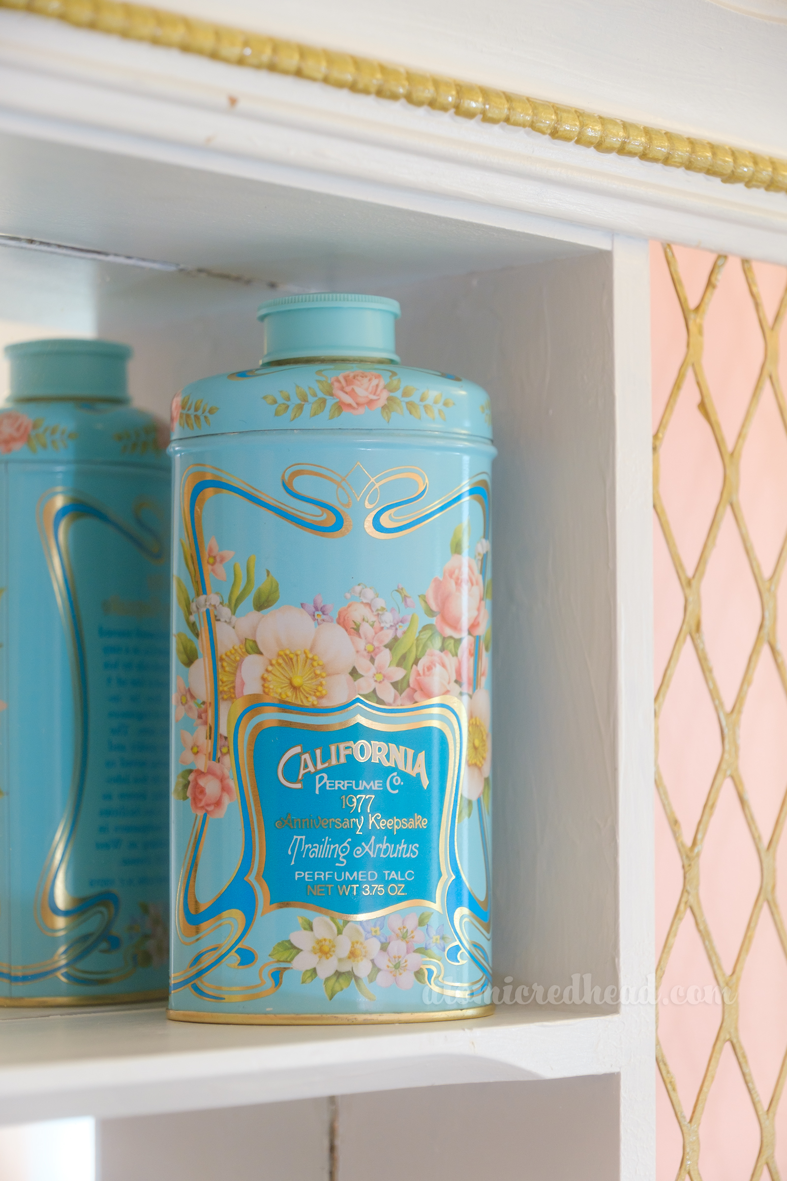 A blue bottle features pink flowers and a darker blue label reading "California Perfume Co. 1977" and sits on a shelf inside the shadowbox.