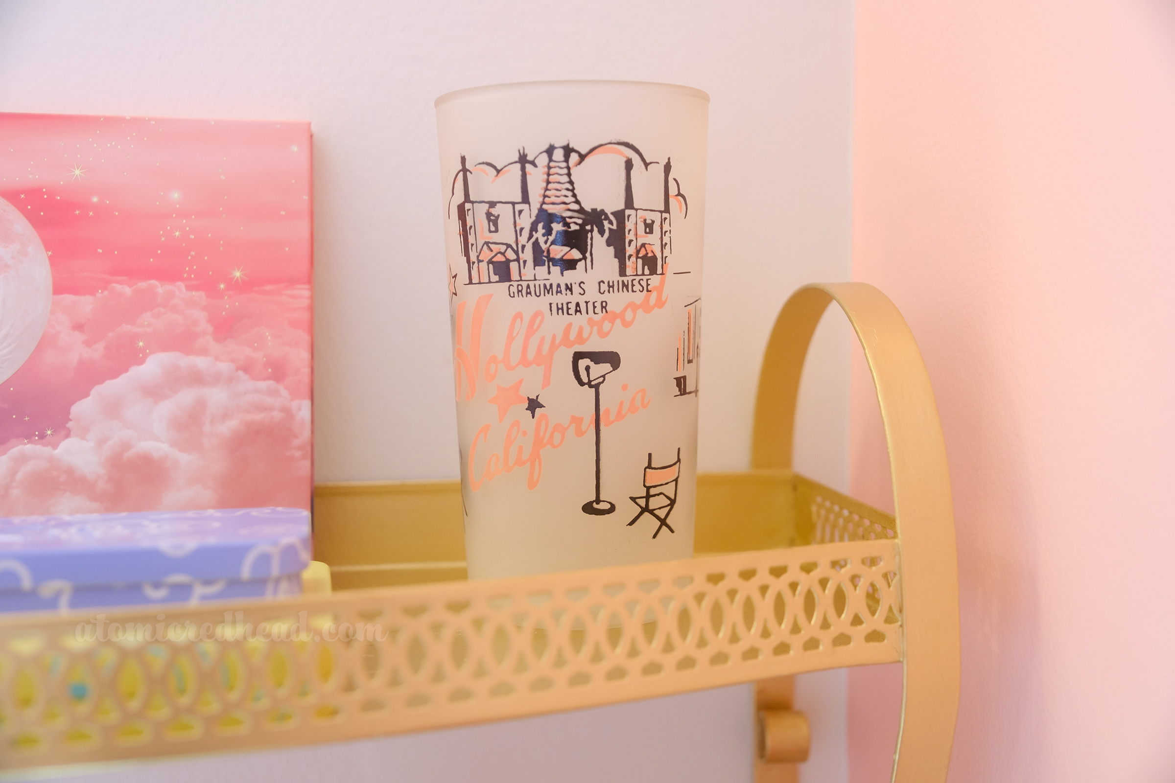 Close-up of a glass that sits on a gold shelf, it reads "Hollywood California" in pink script and features an image of Grauman's Chinese Theater.