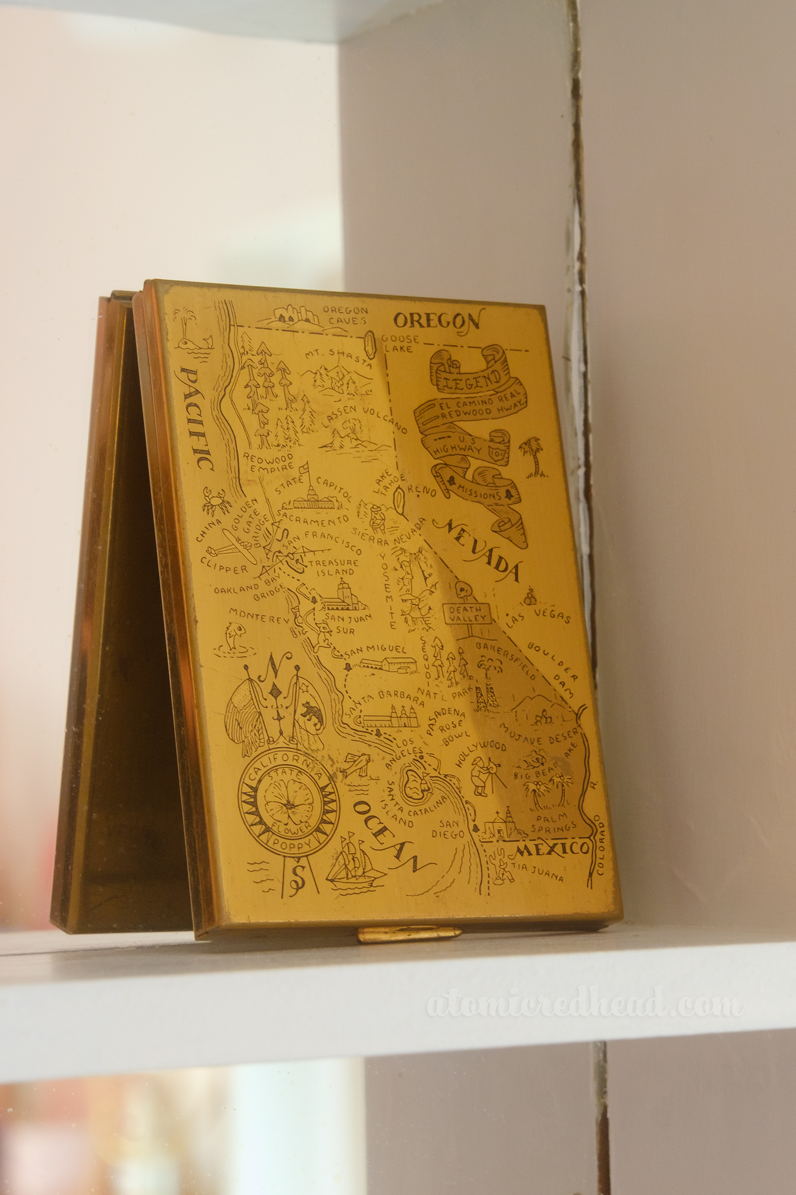 Close-up of a gold tone compact which features a map of California on it.