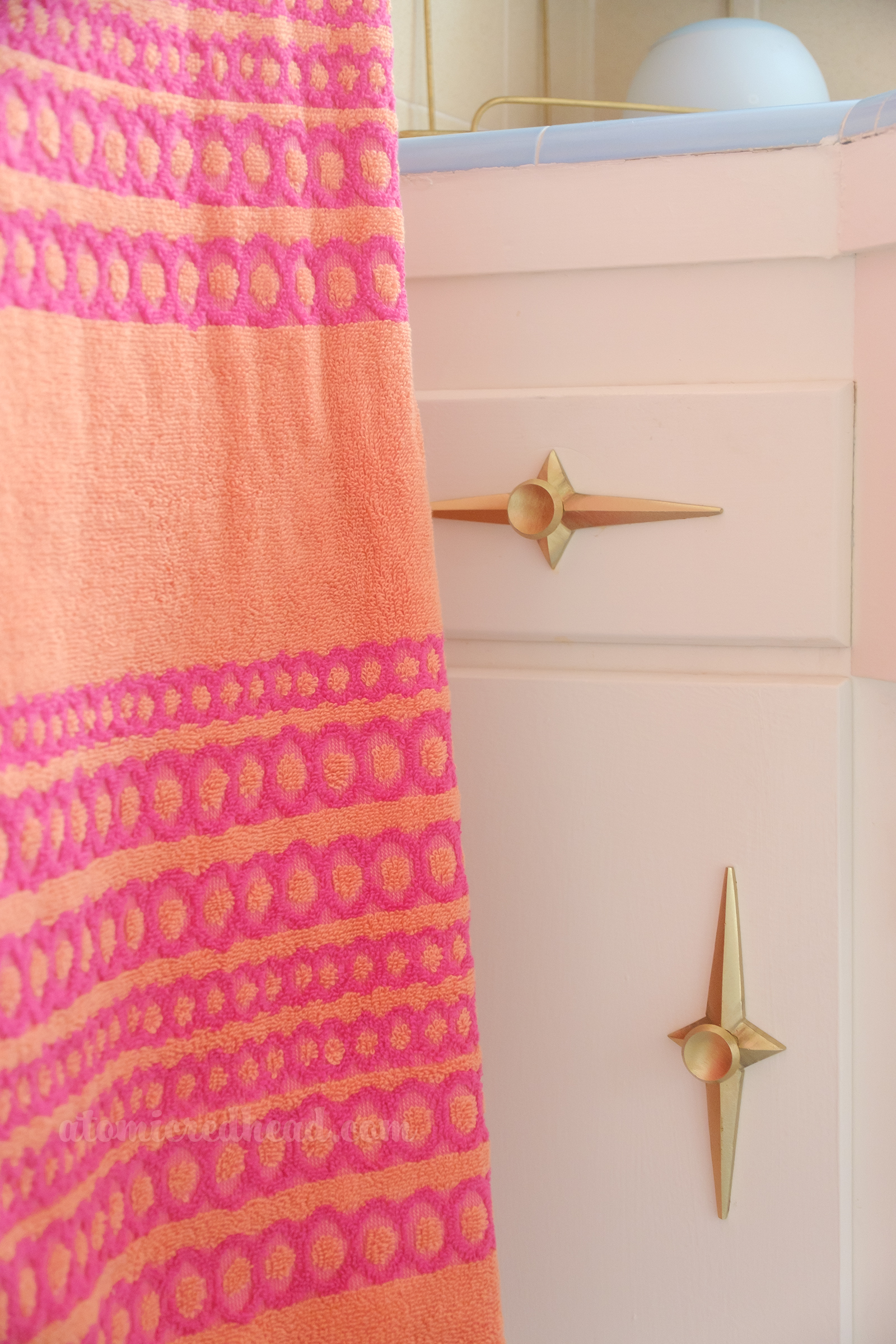 Close-up of a pink and orange towel which rests near the counter and starburst drawer pulls visible on the drawer and cabinet. 