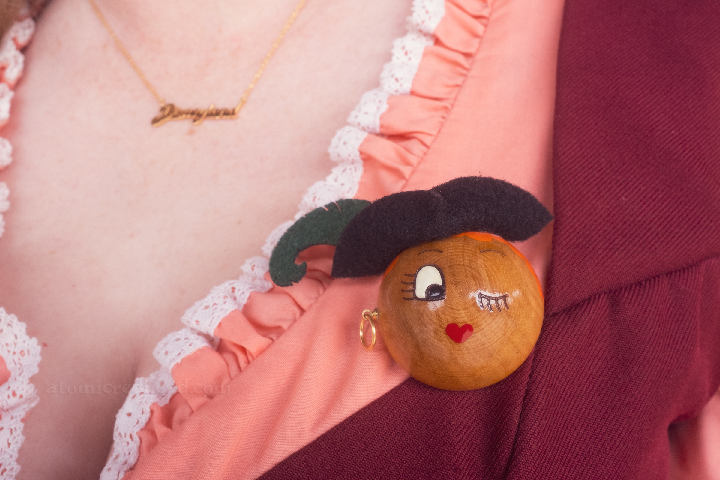 Close-up of my brooch, a wood and felt face of a pirate lass, wearing a black hat with green feather, winking.