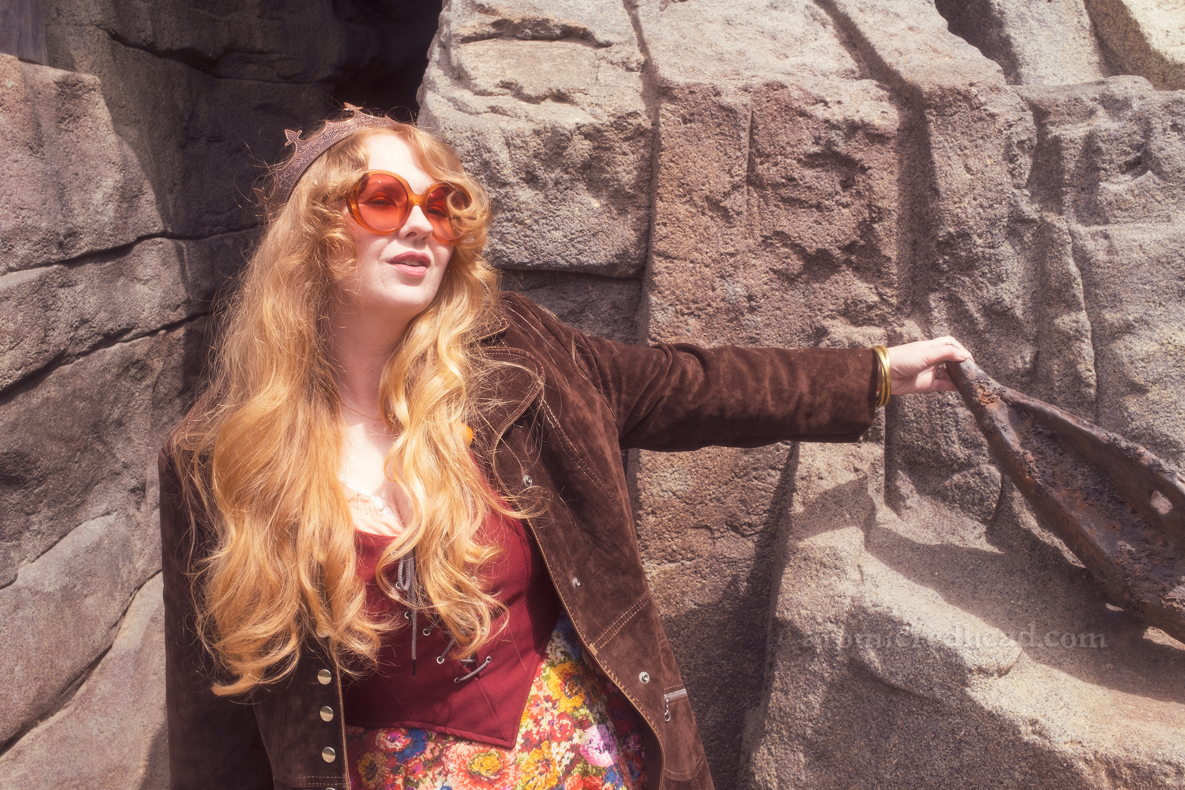 Myself, holding onto a large anchor, leaning away from it, wearing a copper crown, dress with coral sleeves, maroon lace up bodice, and short floral skirt, with a long brown coat over. 
