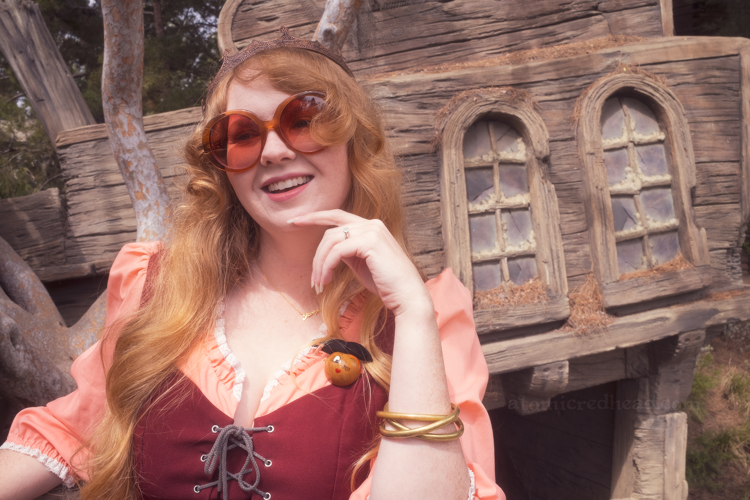 Myself, leaning over a railing, wearing a copper crown, dress with coral sleeves, maroon lace up bodice, and short floral skirt.