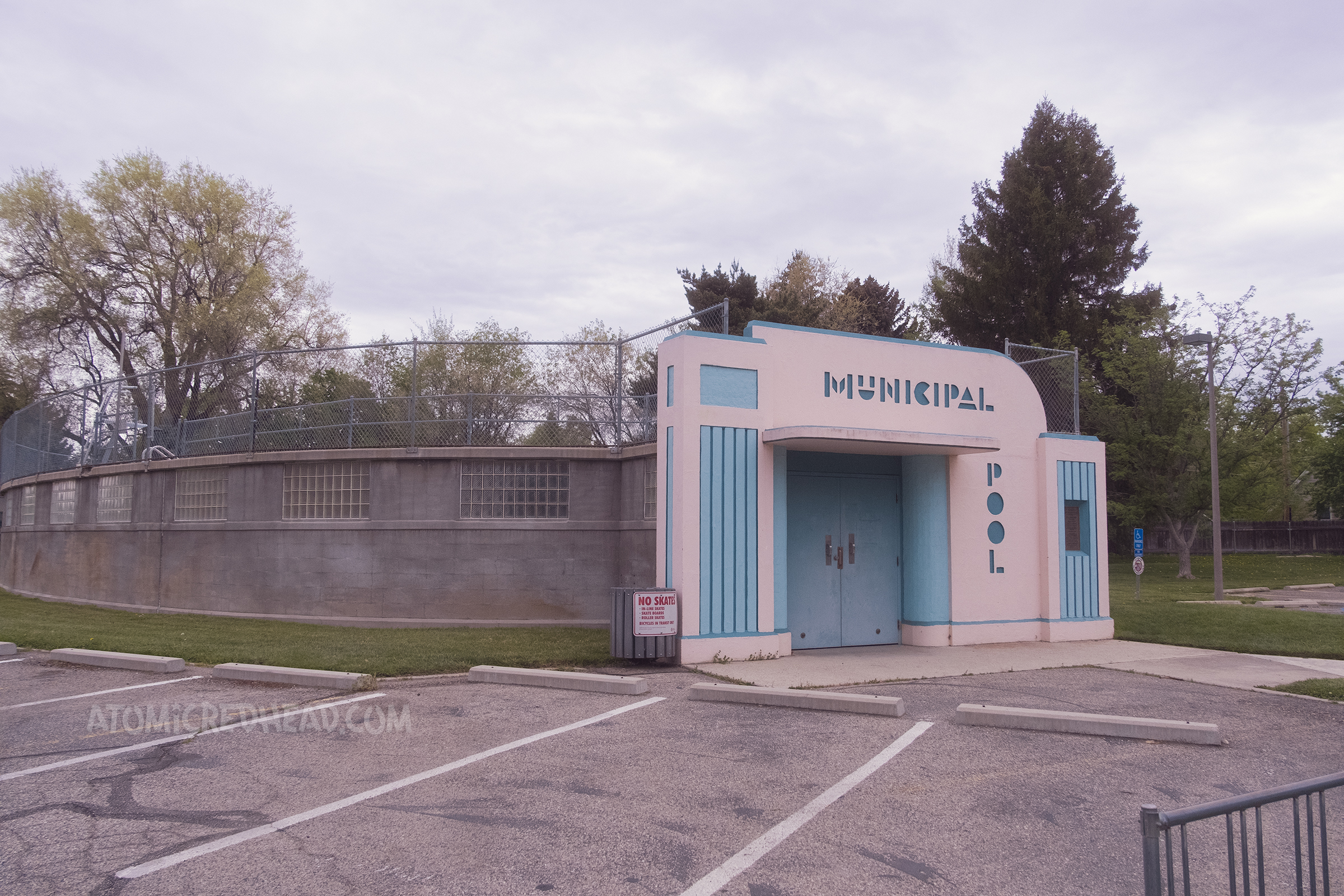 Angled view of the pool, which is above ground, concrete and glass blocks make up the pool walls, with the pink and blue streamline modern doorway to the right.