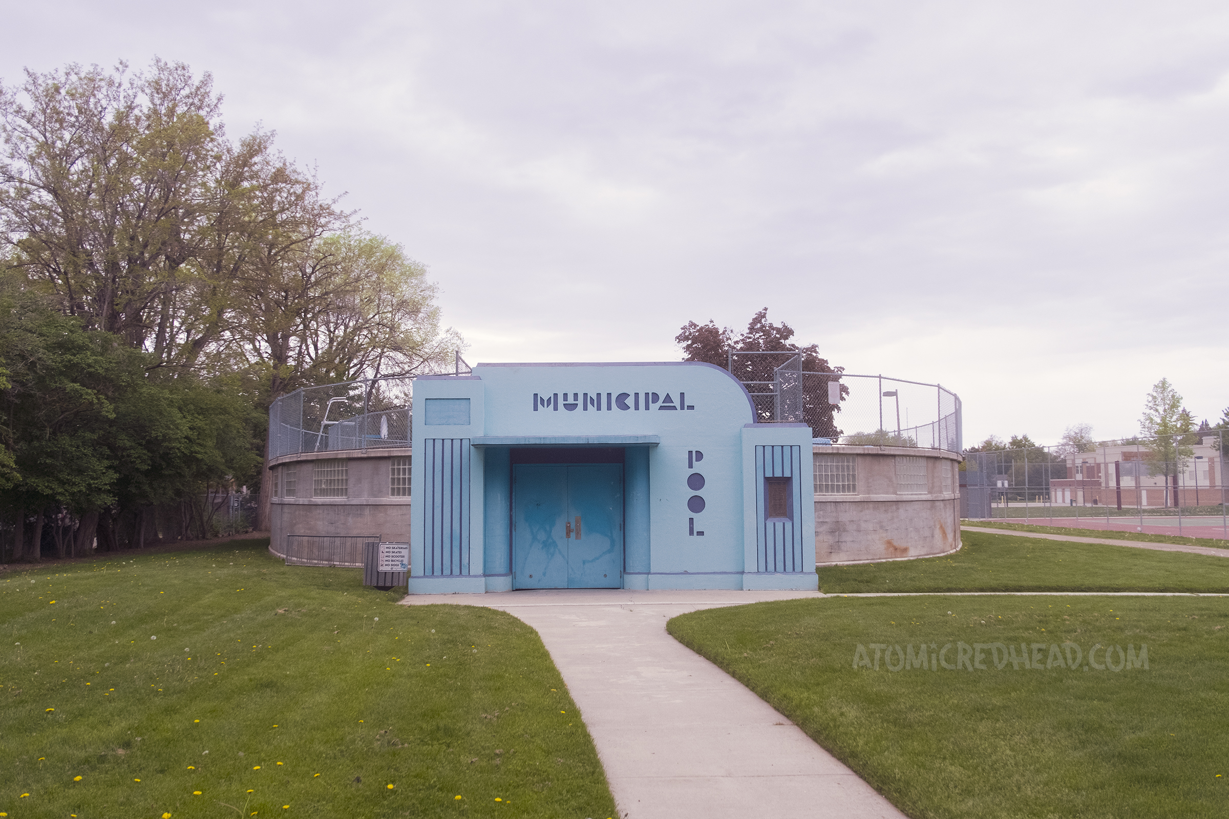 Overall view of the entrance to the streamline moderne pool painted in blue and purple. Above the door reads "Municipal" and to the right of the door reads "Pool"