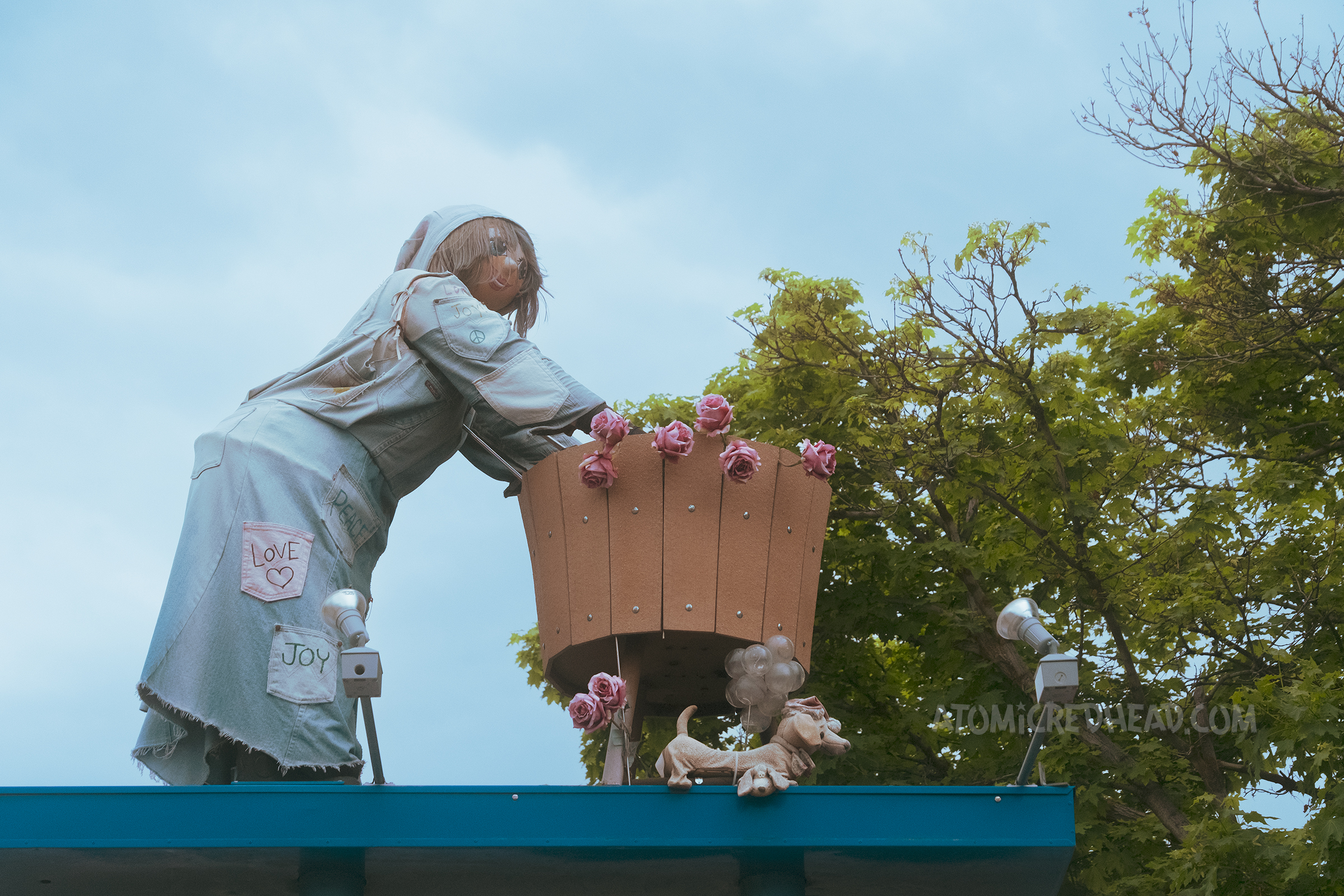 Close-up of the washer woman, who wears a denim outfit and roses hang from her wash tub.