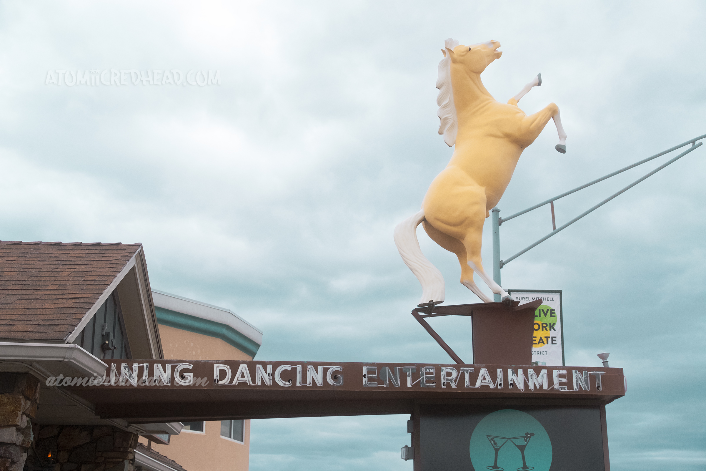 A rearing horse stands atop an awning for a building, on the side of the awning reads "Dining Dancing Entertainment" in neon.