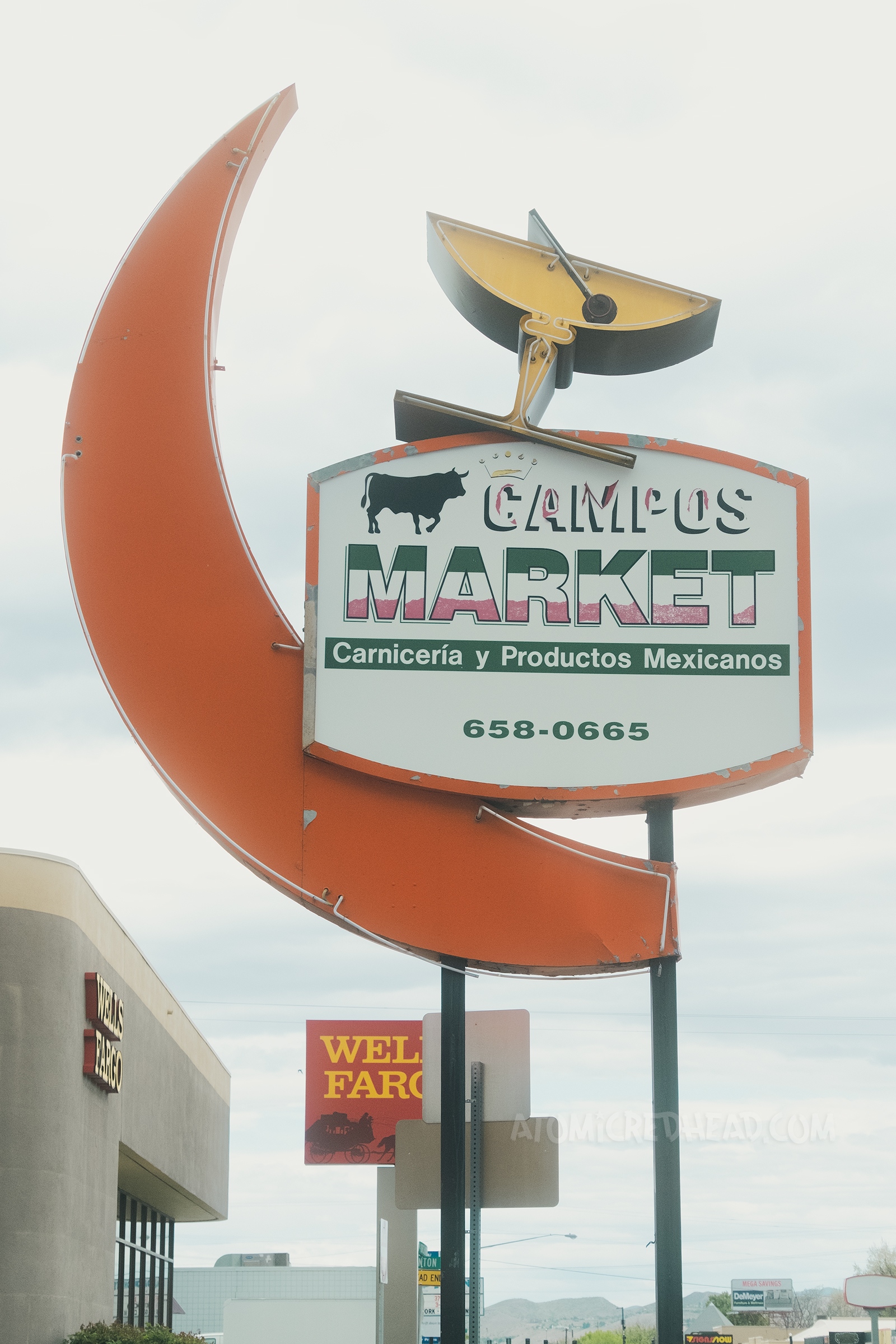 An orange crescent moon makes up part of a sign that also has a cocktail glass on top, all neon, with a backlit plastic sign reads "Compos Market"