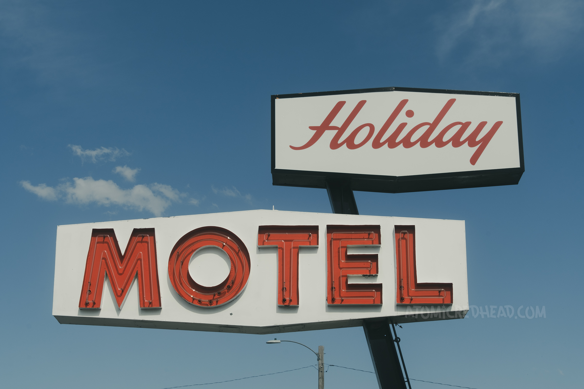 A combination neon and backlit plastic sign reads "Holiday Motel" in red and white.