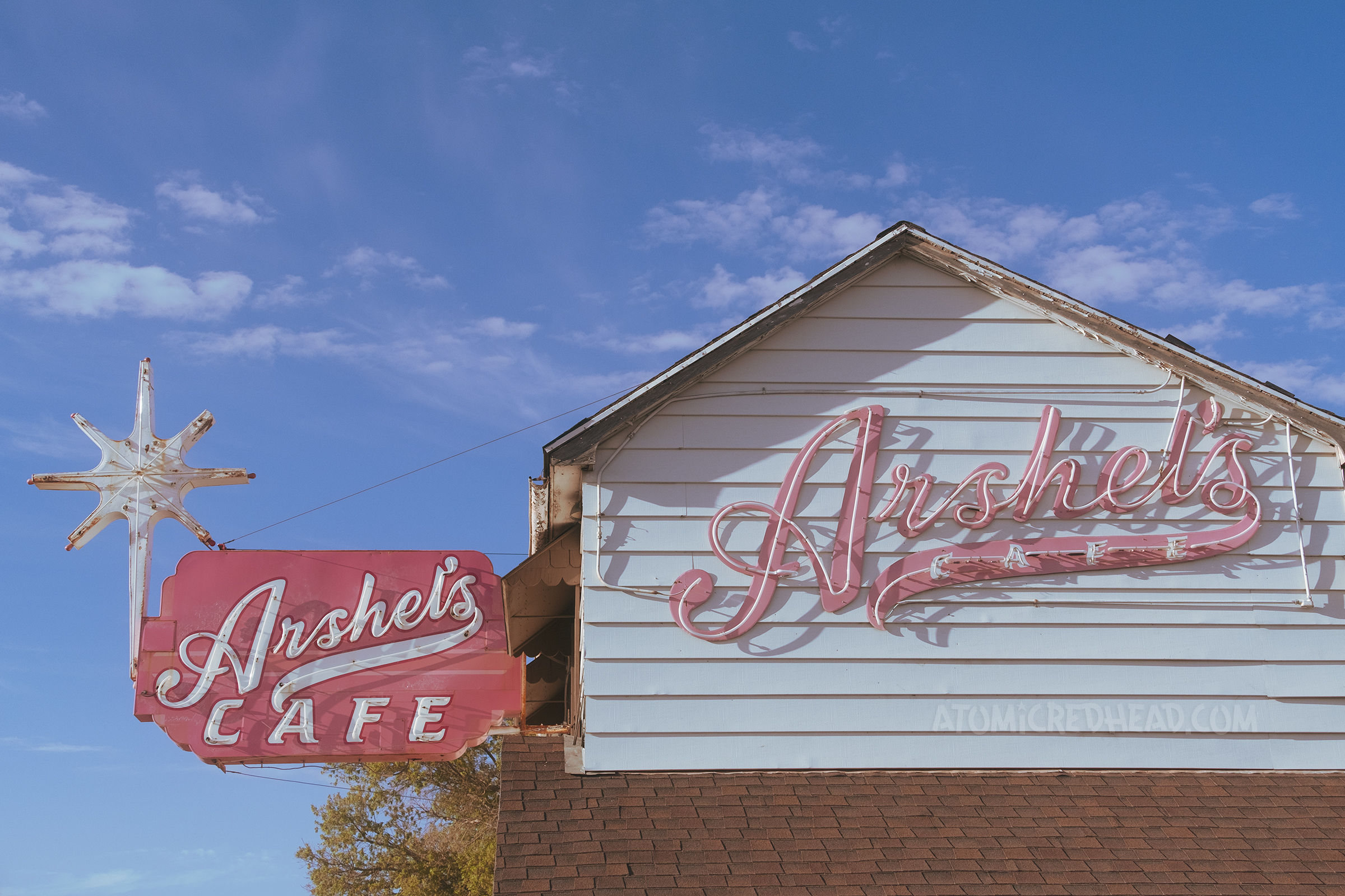 A large red and white neon sign reads "Arshel's cafe" in script and has a neon star on the left. Across the side of the building in red neon script reads "Arshel's Cafe"