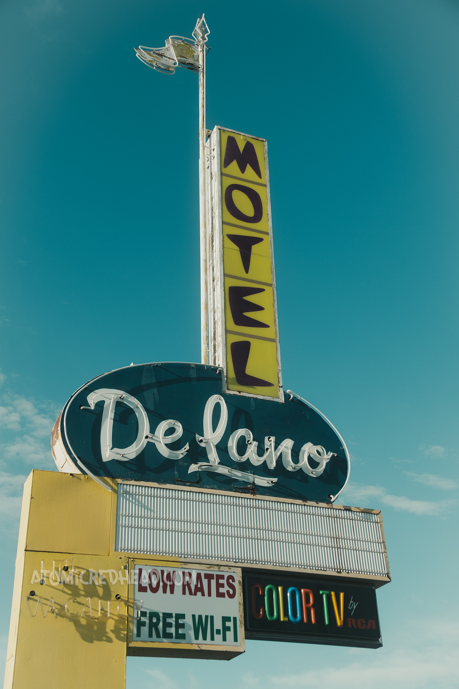 Combination backlit plastic and neon sign, reading "Motel" in black letters on yellow to a blue oval reading "De Lano" in white script neon.