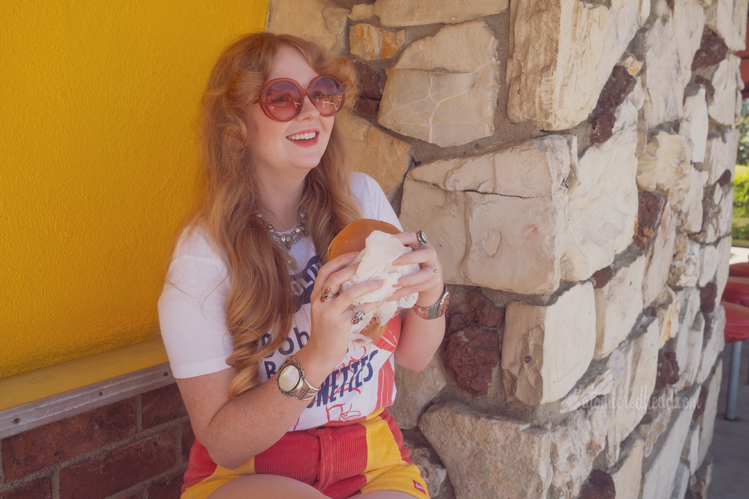 Myself seated at a barstool against the bright wall of the Munch Box, eating a burger, wearing a shirt reading "From Hollywood Bob Baker's Marionette's" and features a clown marionette, 