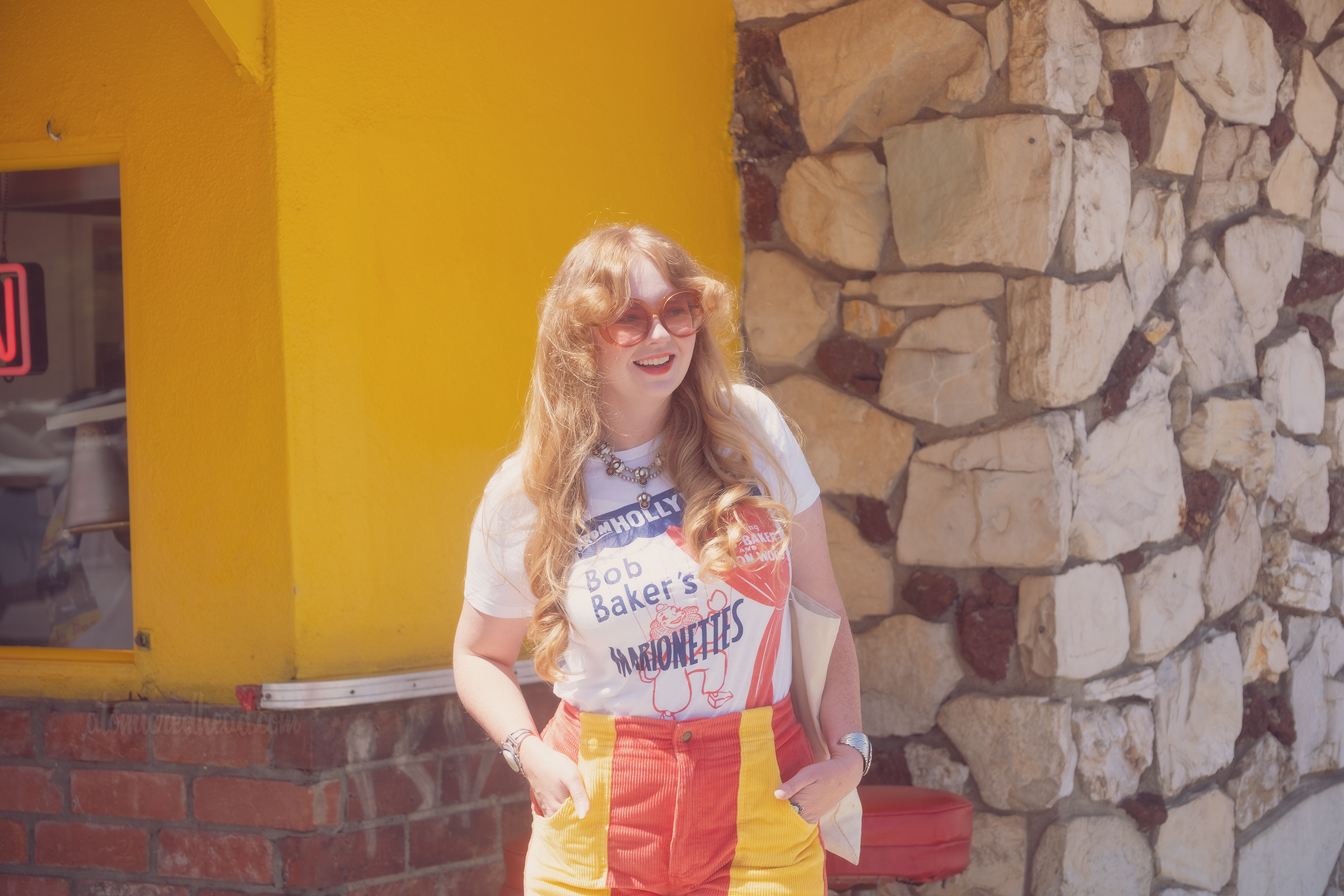 Myself standing outside of the bright yellow and red Munch Box building, wearing a white shirt with a clown marionette on it and text reading "From Hollywood Bob Baker's Marionettes" and red shorts with yellow pockets.