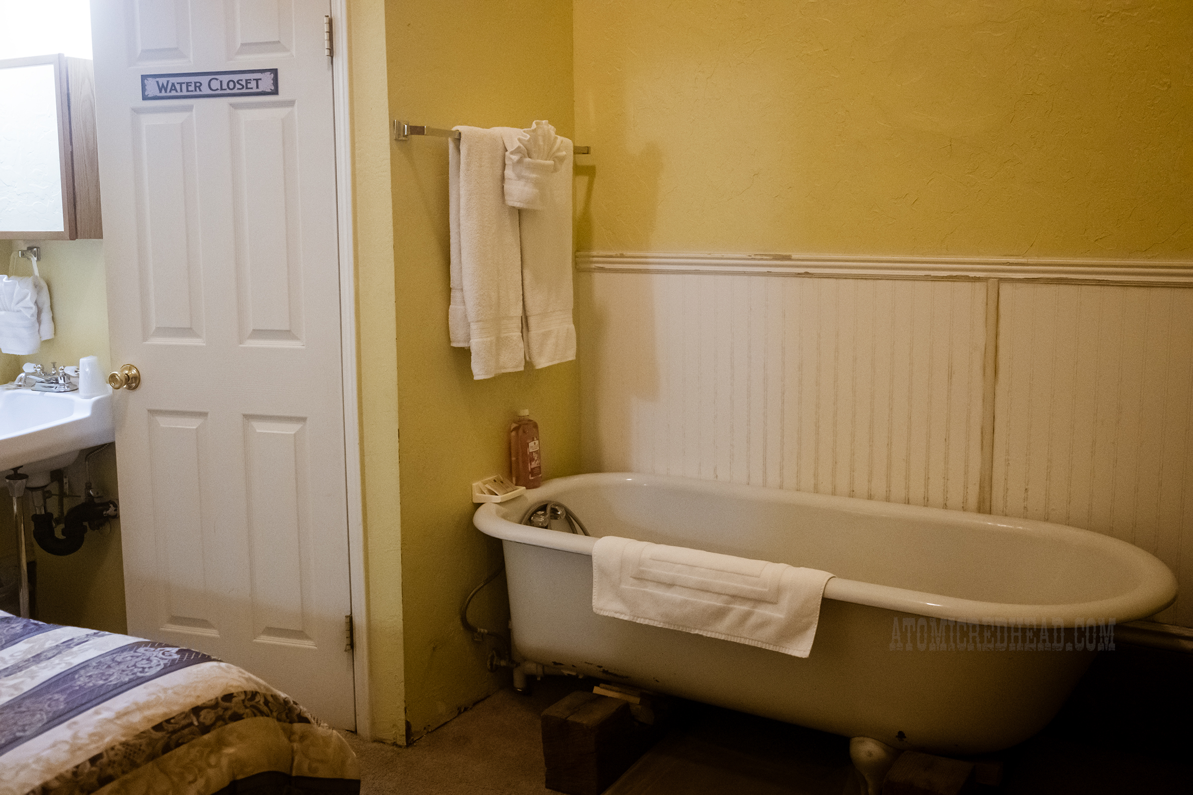 A claw foot bathtub sits against a white and yellow wall.
