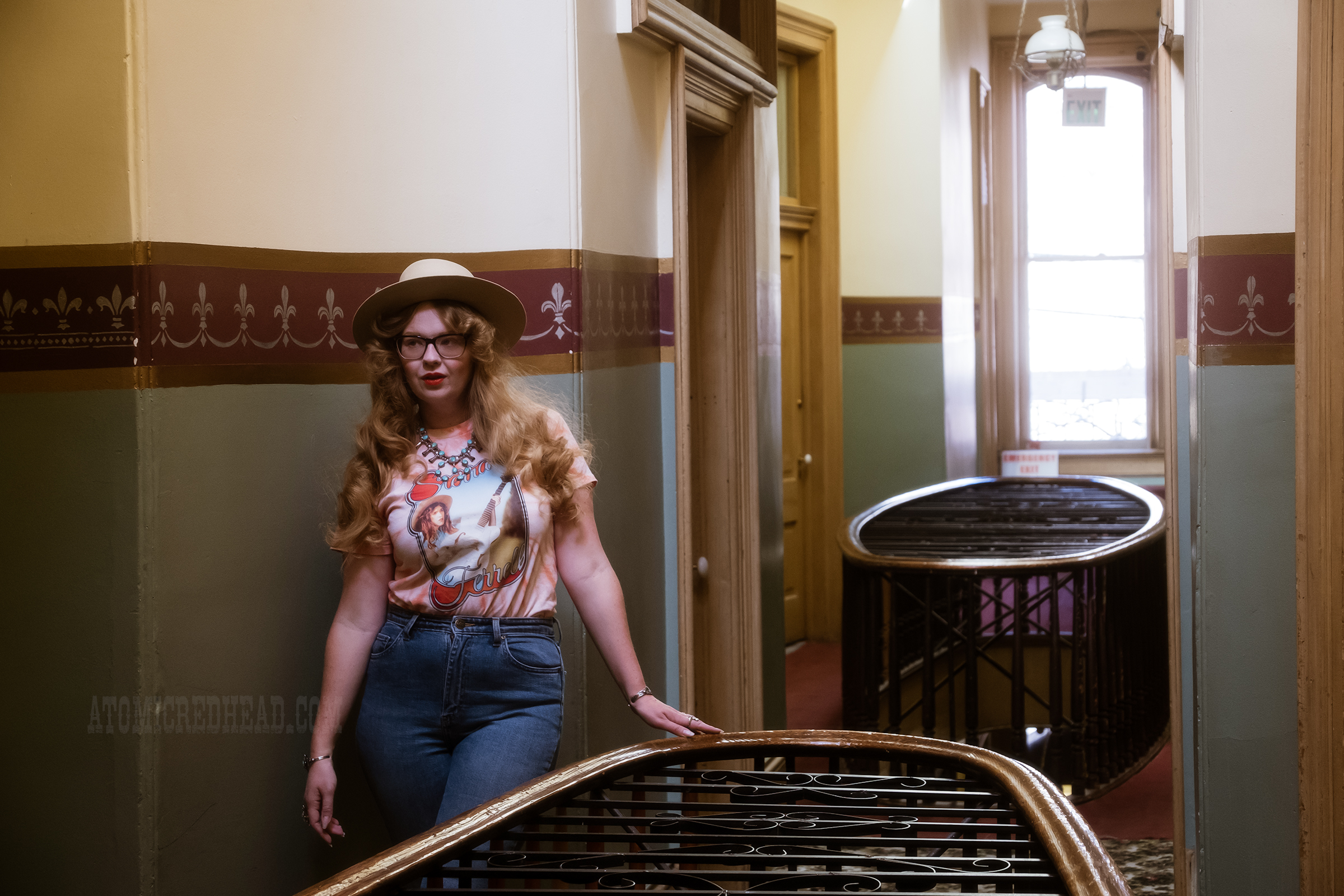 Myself standing against the railing of the second floor overlook, wearing a cream cowboy hat, peach tie dye shirt featuring musician Sierra Ferrell. 