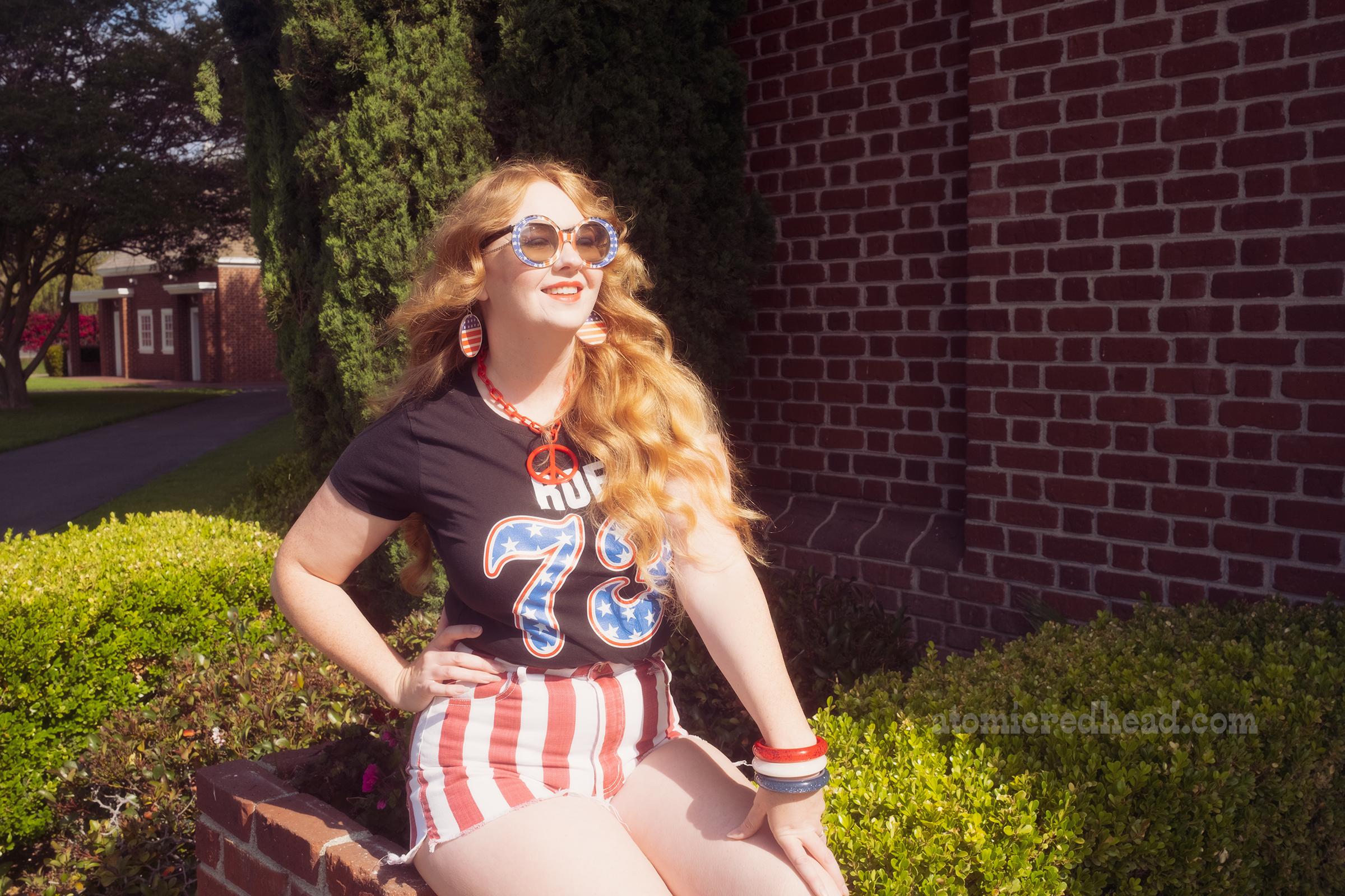 Myself, wearing sunglasses that feature the American Flag, a black shirt reading "Roe 73" with the "73" in blue with white stars, edged in red, a red and white stripe shorts, sitting on a planter near Independence Hall.