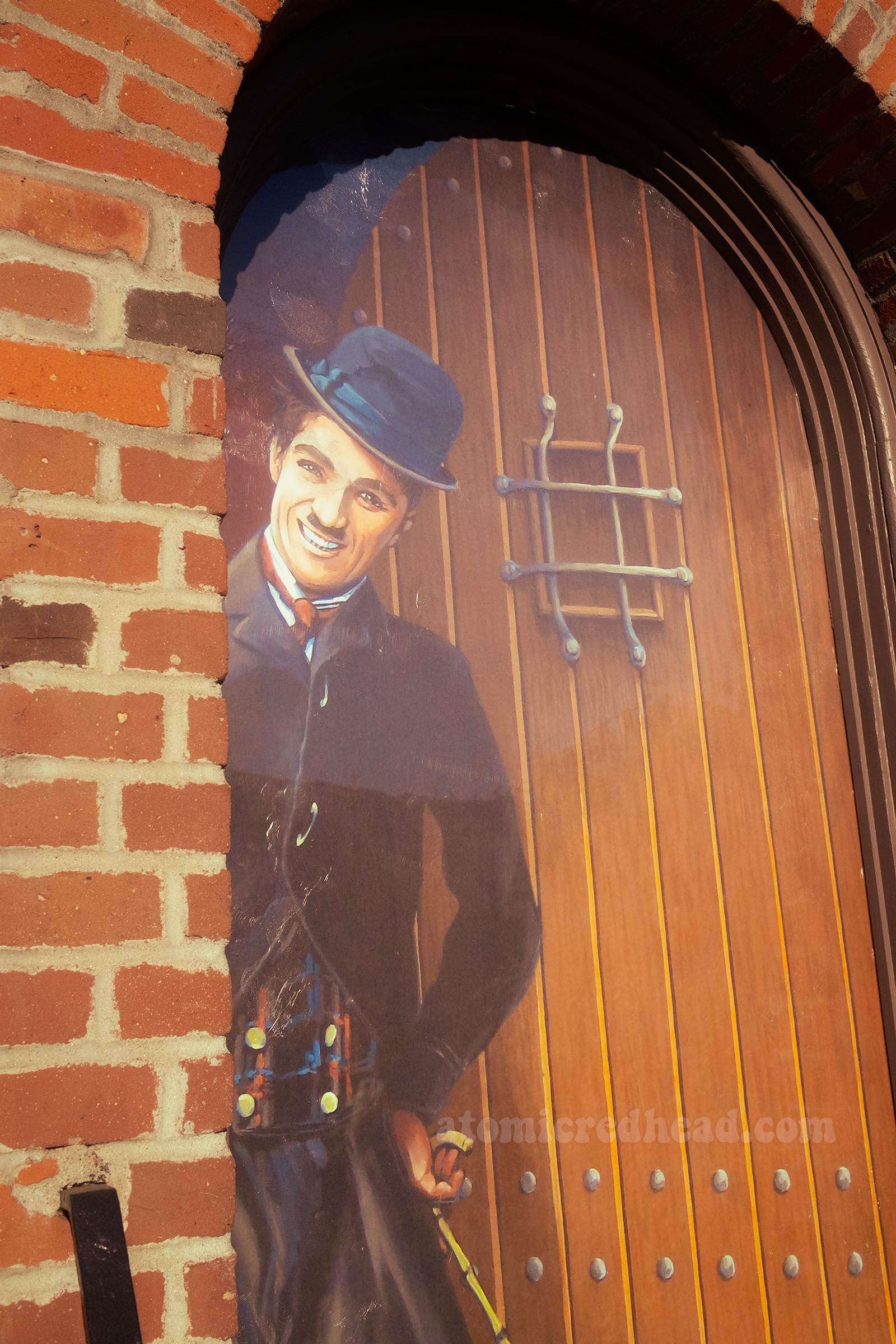 A door is painted with the image of Charlie Chaplin dressed as The Tramp, in a black suit, bowler hat, and bamboo cane.