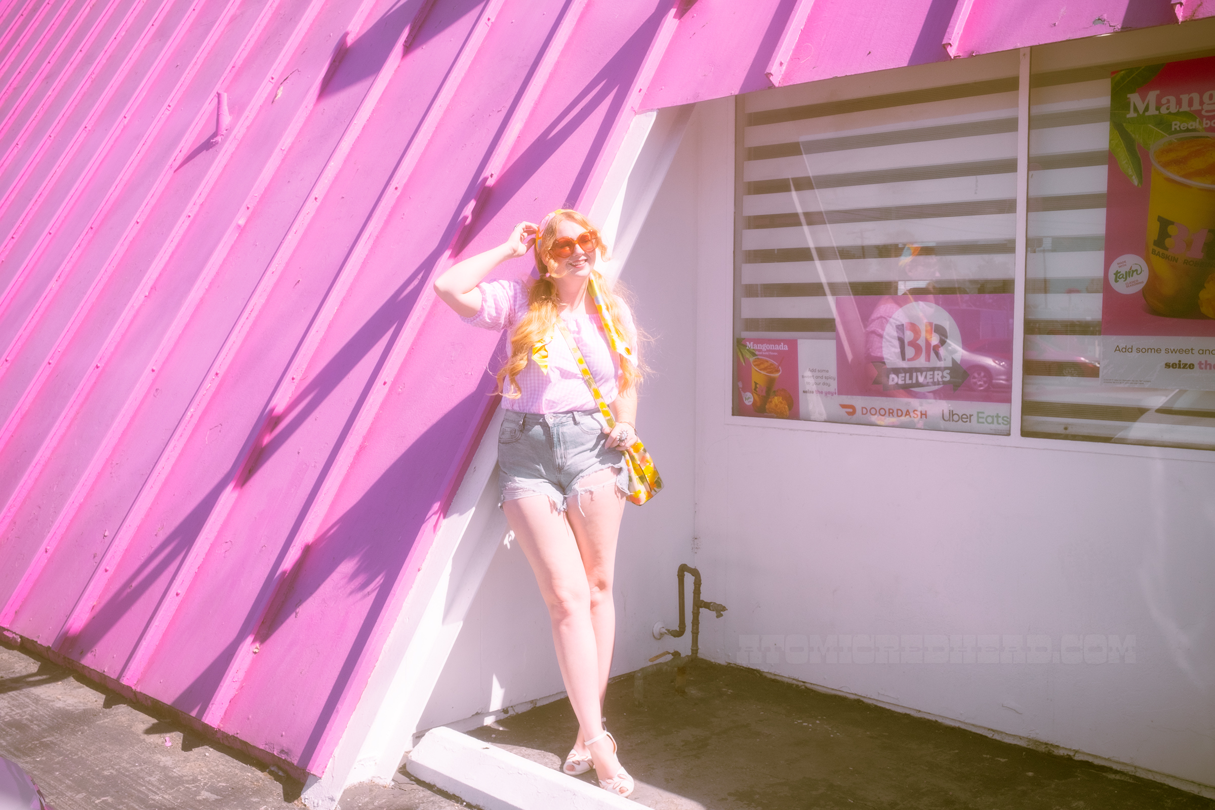 Myself standing in front of the location, wearing a pink and white gingham peasant blouse and jean shorts.