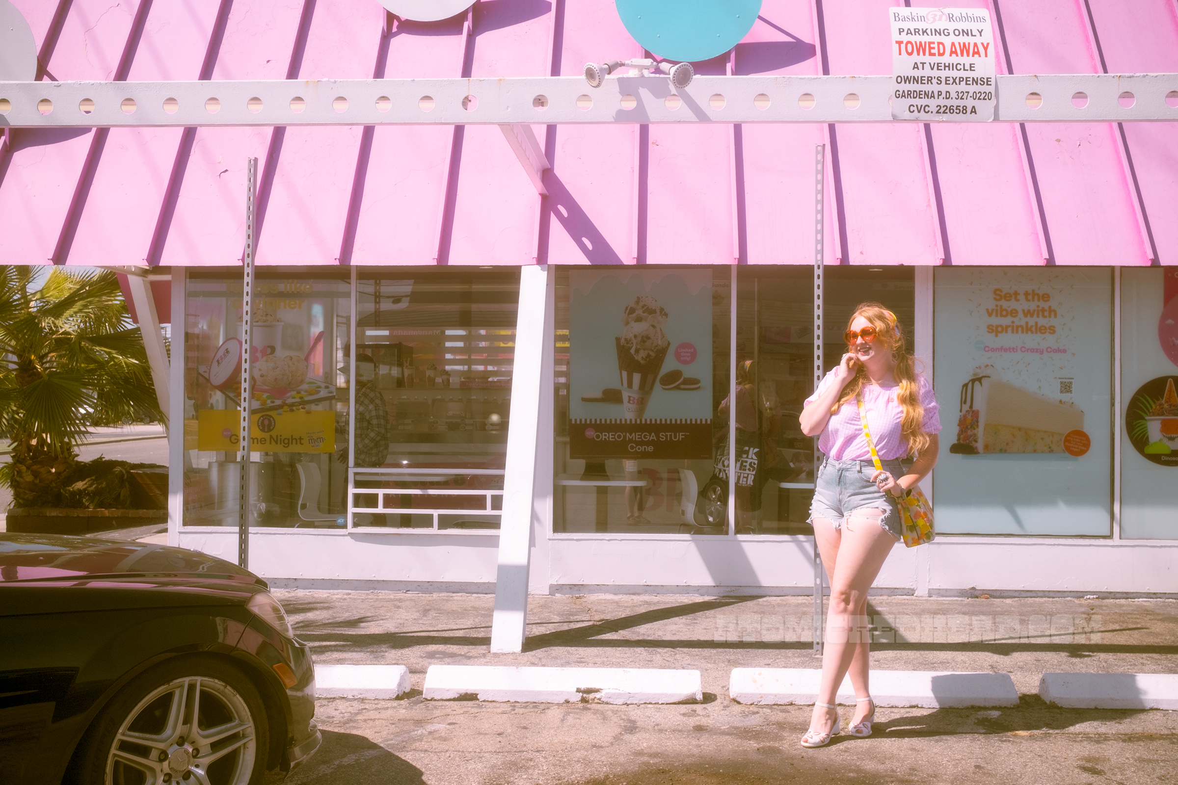 Myself standing in front of the location, wearing a pink and white gingham peasant blouse and jean shorts.
