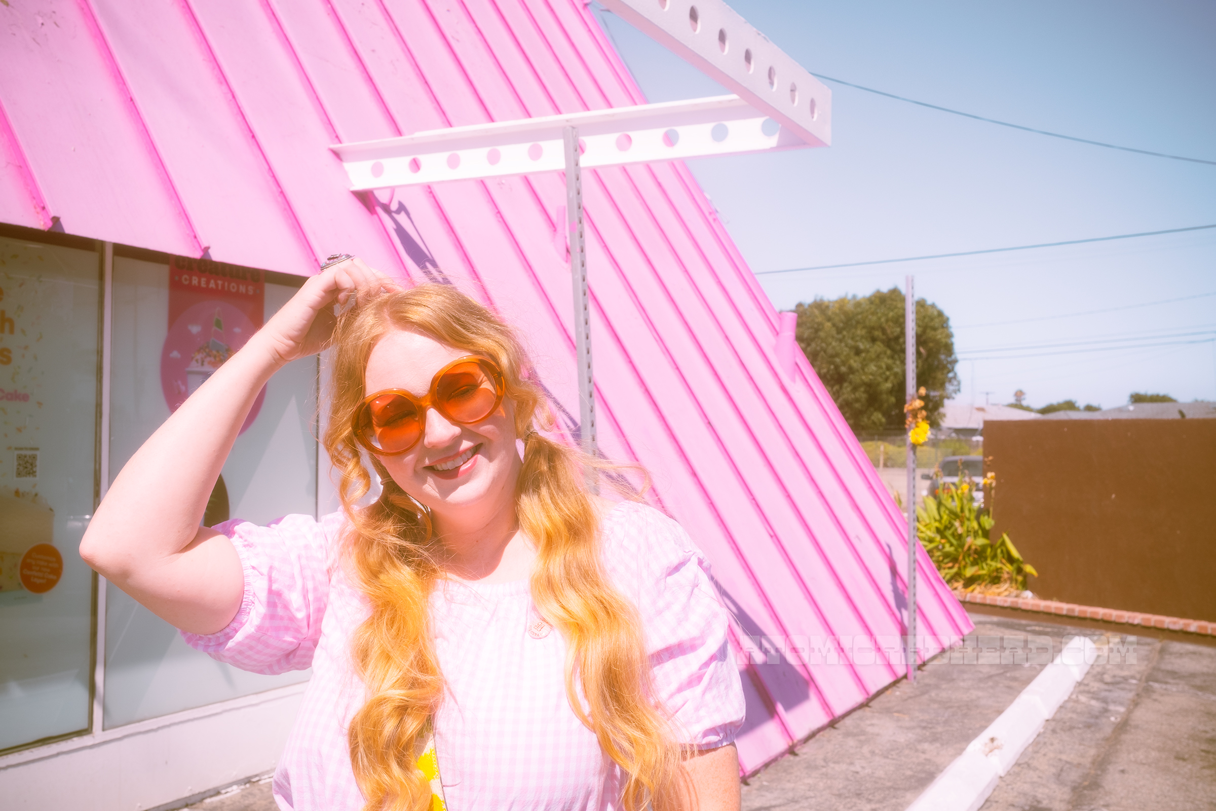 Myself standing in front of the location, wearing a pink and white gingham peasant blouse and jean shorts.