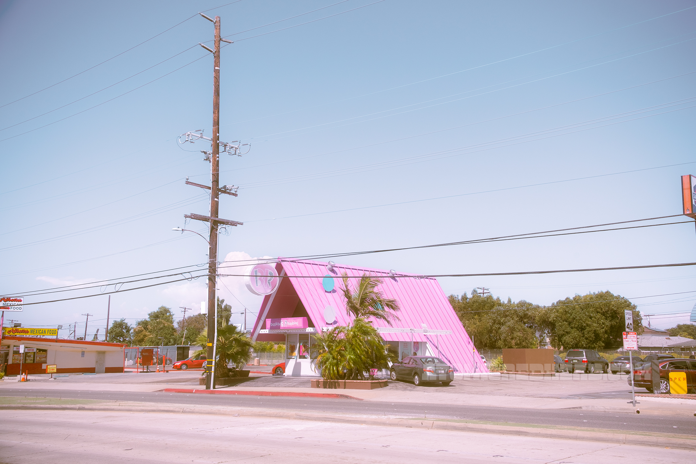 Overall, angled view of the Baskin Robbins, with its pink roof and palm trees out front.