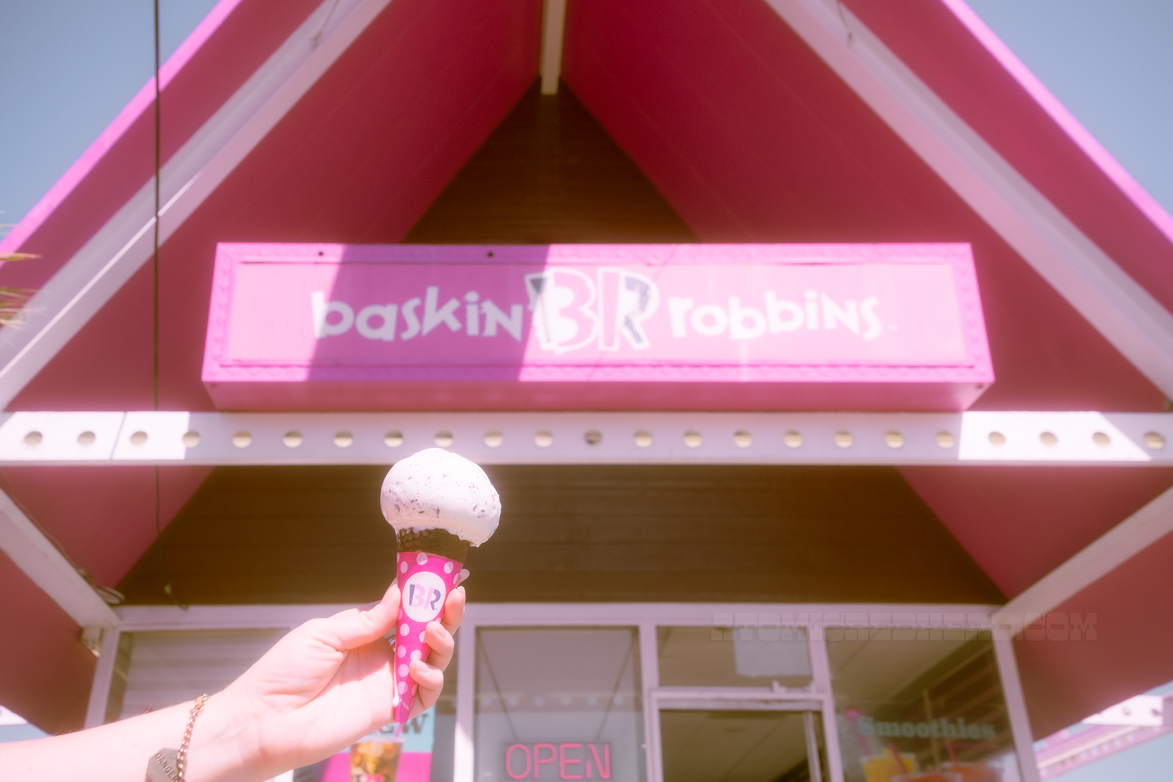 A scoop of Mint Chocolate Chip on a cone outside of the shop, with the sign reading Baskin-Robbins in the background.