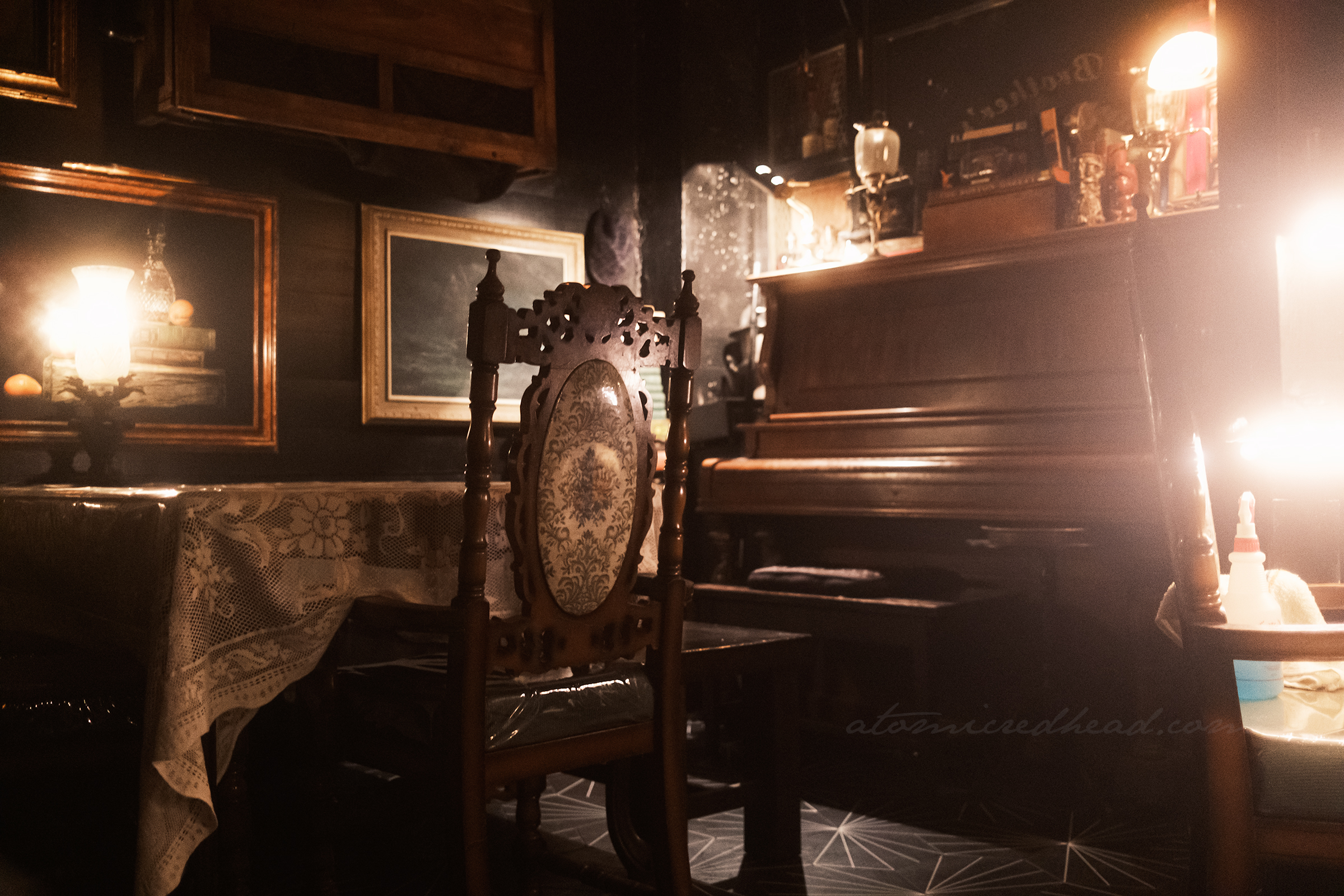 Interior of Blind Rabbit, various antiques scattered, a table with a lace tablecloth, piano and pictures hang on the wall.